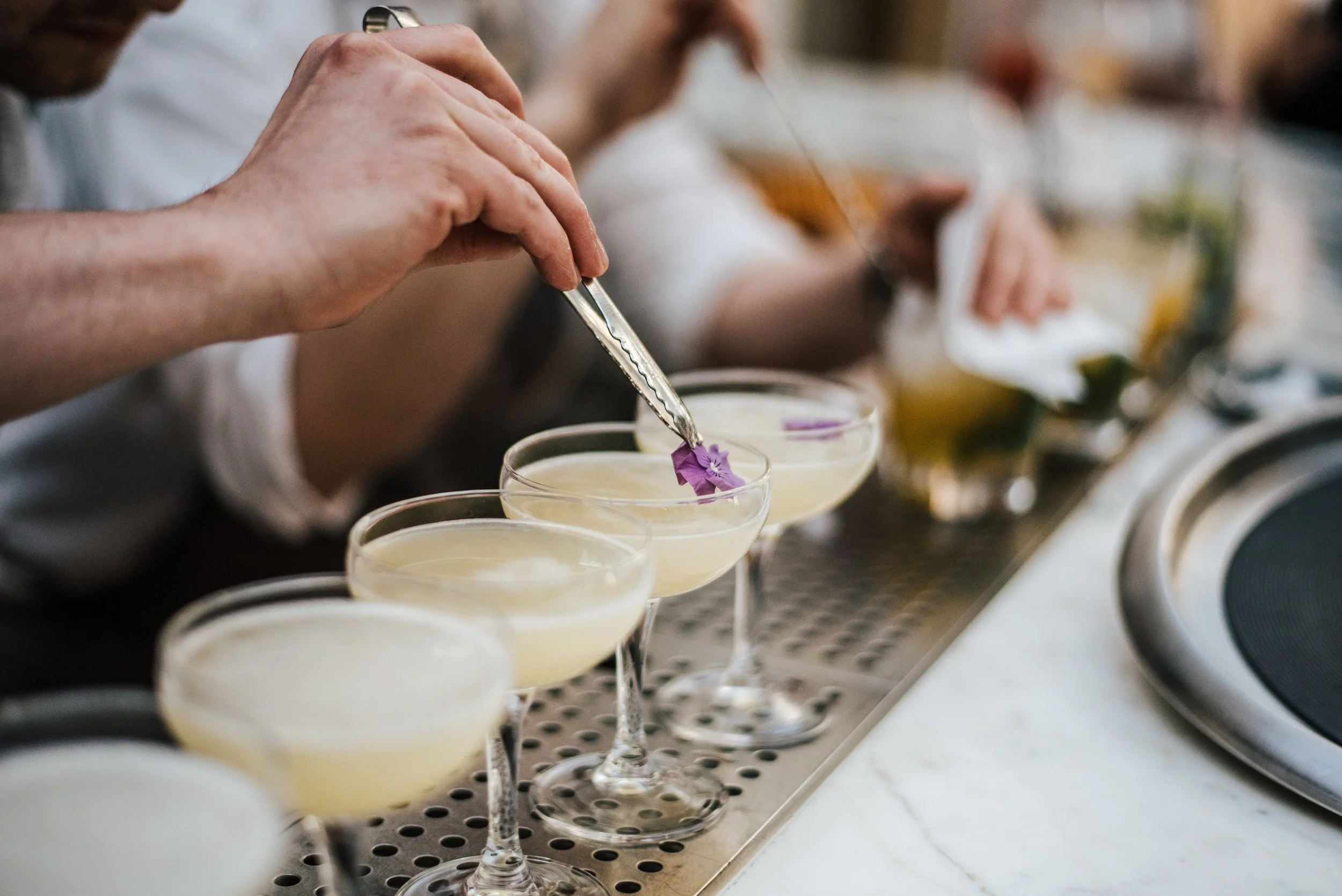 Verres à cocktail avec une décoration florale, alignés sur un plateau en métal.