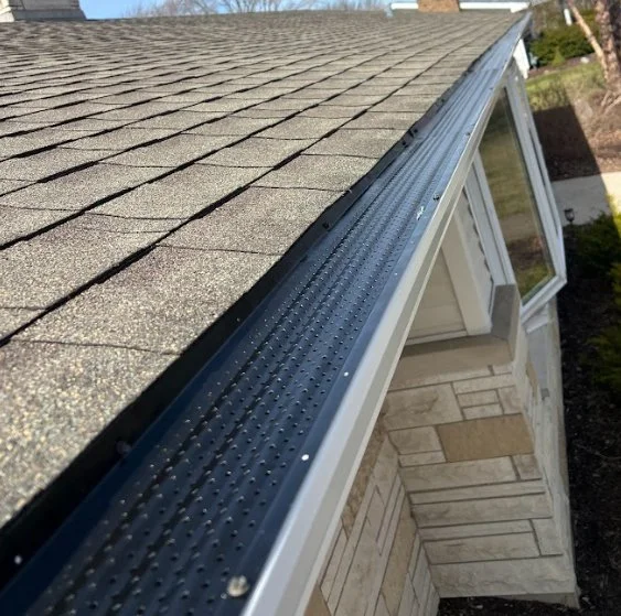 Close-up of a house roof with asphalt shingles and gutter system with leaf protection.