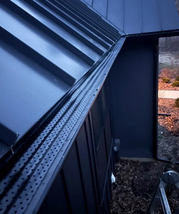 Close-up of a modern black metal building exterior with a gutter with Bulldog leaf protection system.