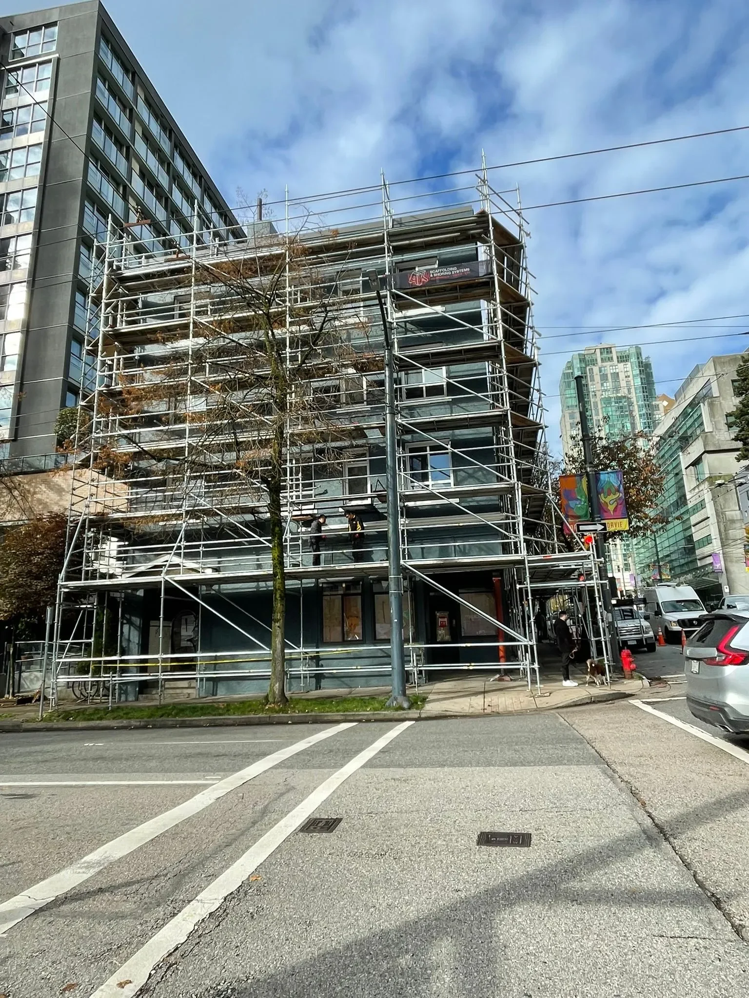 Building under renovation with metal scaffolding, pedestrians, and parked cars, painted and maintained by painters offering free painting estimate and exterior painting services near you.