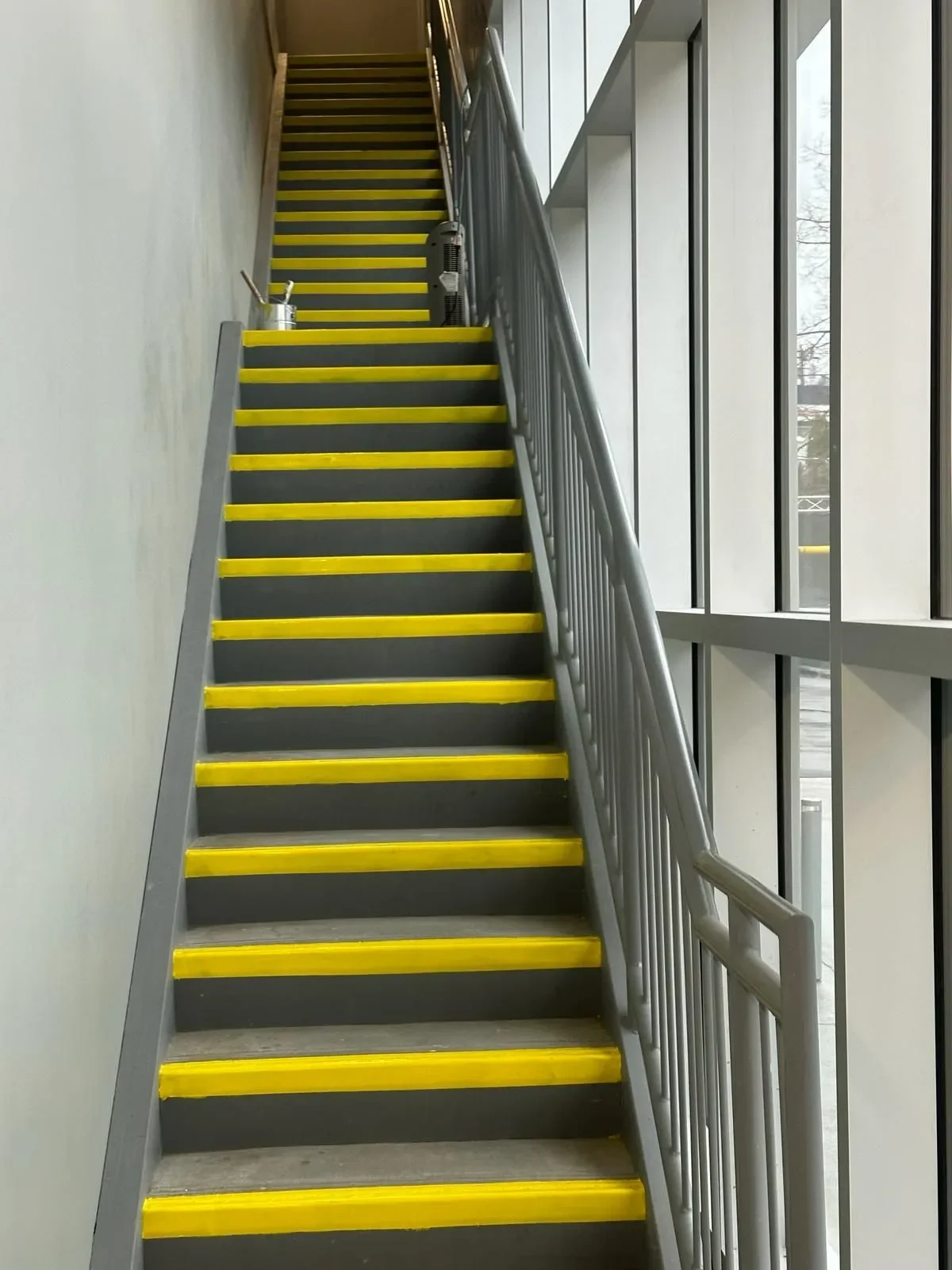 Interior staircase with black steps and yellow safety strips by large windows, painted and maintained by professional painters offering free painting estimate and interior painting services near you.