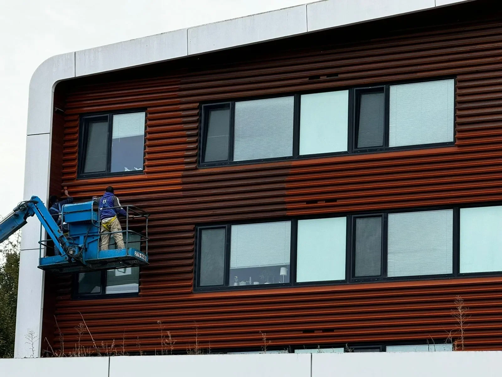 Professional painters on a blue lift completing exterior painting on a modern commercial building, offering free painting estimate and exterior painting services near you.
