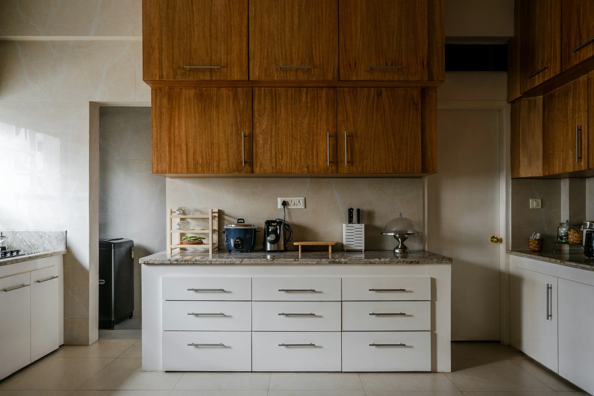 Kitchen with white lower cabinets, wooden upper cabinets, granite countertops, a small rack with dishes, small appliances on the counter, and a closed door.