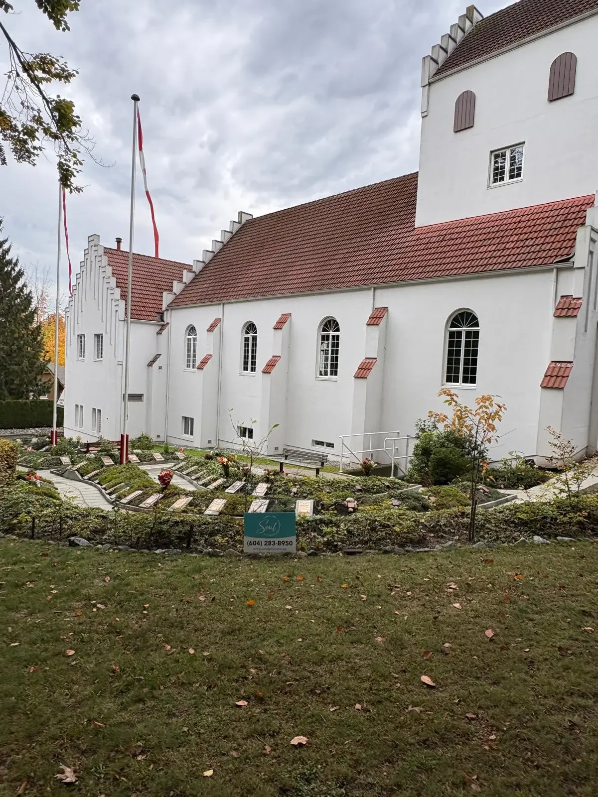 White church with red-tiled roof, arched windows, and flags, surrounded by landscaped garden, painted and maintained by painters offering free painting estimate and exterior painting services near you.