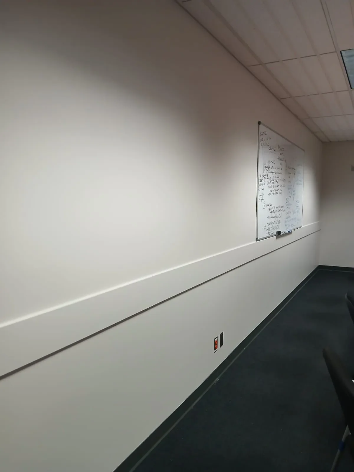 Classroom with whiteboard, tile ceiling, black carpeted floor, and chairs, painted and maintained by painters offering free painting estimate and interior painting services near you.