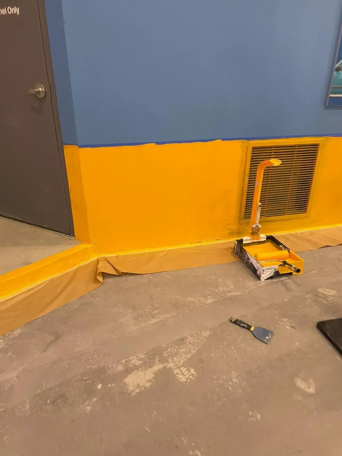 Interior wall being painted blue and yellow by professional painters, with paint roller and tray, offering free painting estimate and interior painting services near you.