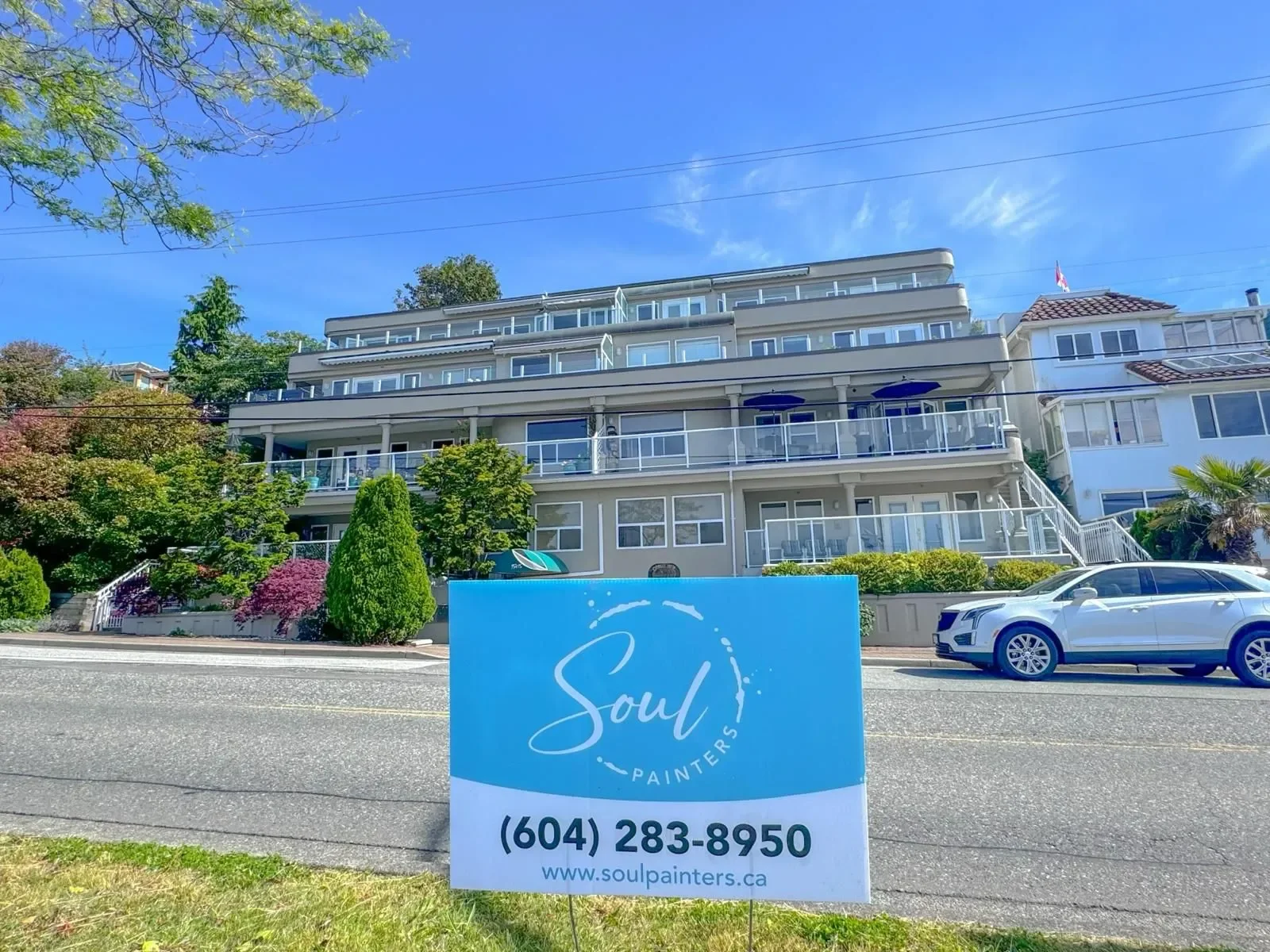 Multi-story residential building with balconies, surrounded by trees and shrubs, with a sign in the foreground for Soul Painters displaying contact information and website.