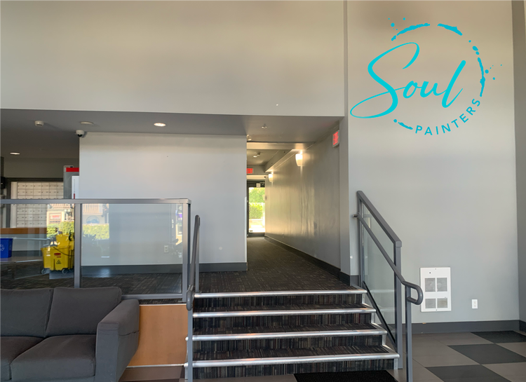 Interior of modern building with staircase to upper level, gray sofa, and large blue "Soul Painters" logo on wall, painted and maintained by painters offering free interior painting estimate near you.