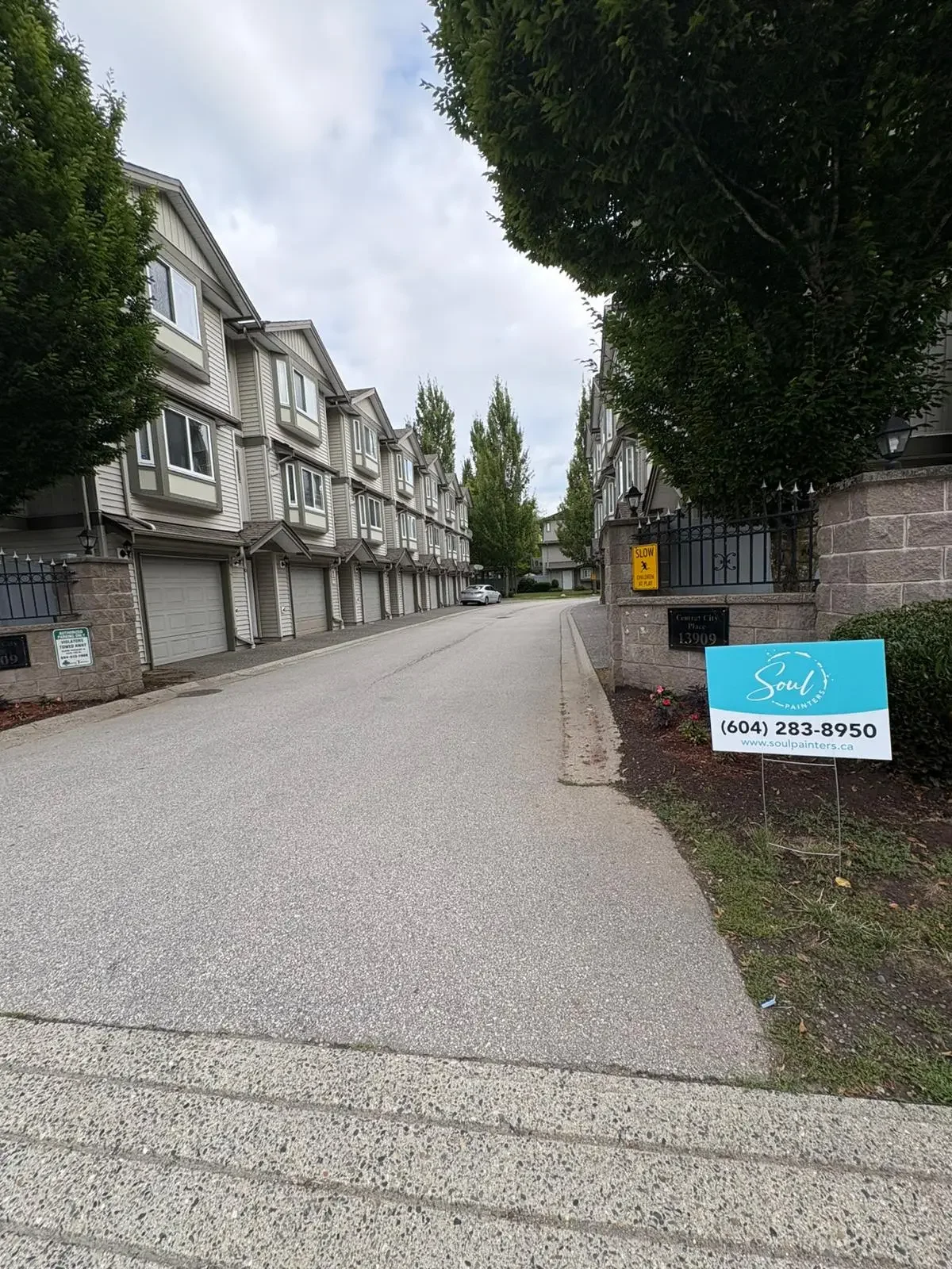 A residential street with multi-story townhouses on the left and a sign for Soul Painters on the right, with trees lining the street and overcast sky.