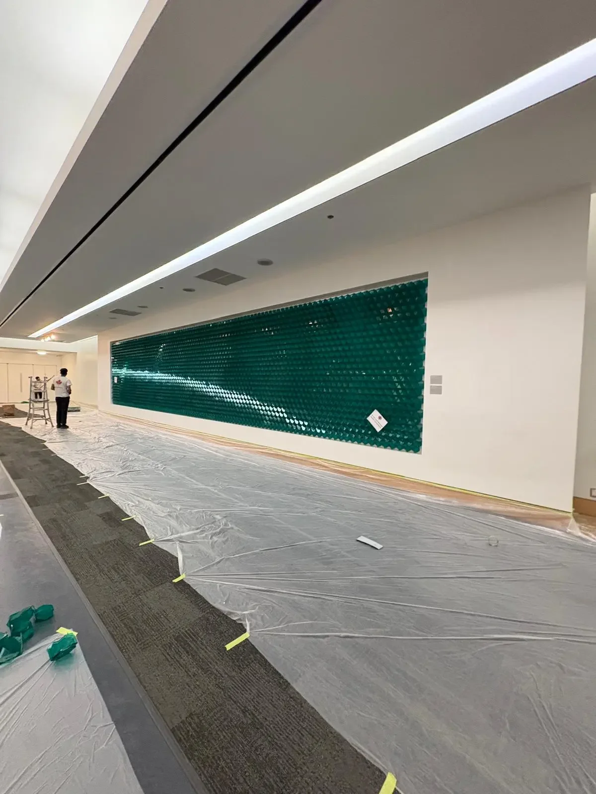 Painters installing a green mosaic wall in an indoor space with white walls and ceiling, offering free painting estimate and interior painting services near you.