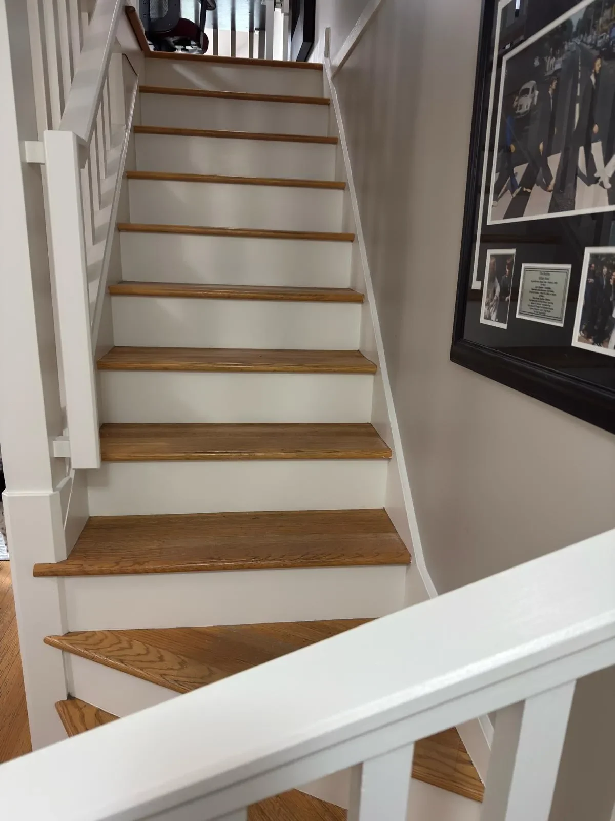 Interior view of a staircase with wooden steps and white railings in Burnaby, next to a wall with framed photographs.