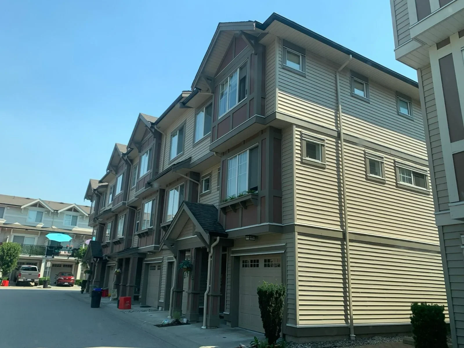 Multi-story residential townhouse complex with beige siding and small front porches, situated in a sunny neighborhood.