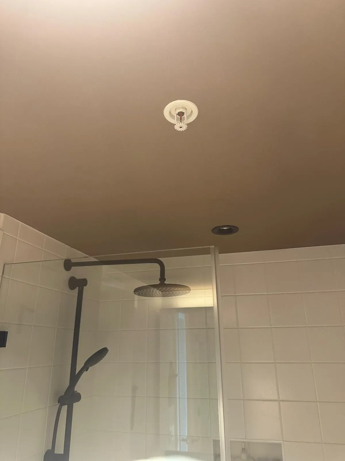 Bathroom ceiling with smoke detector and shower area with rain shower head in Langley.