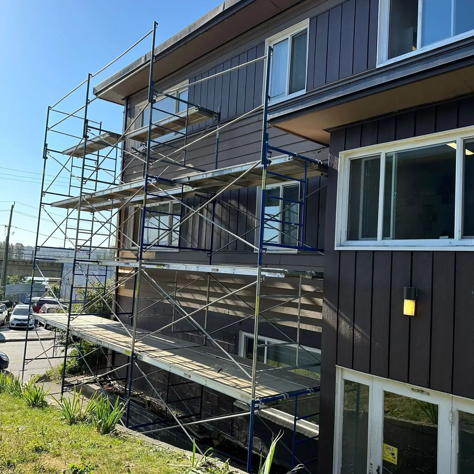 Construction scaffolding set up on the side of a dark-colored building with white window frames.