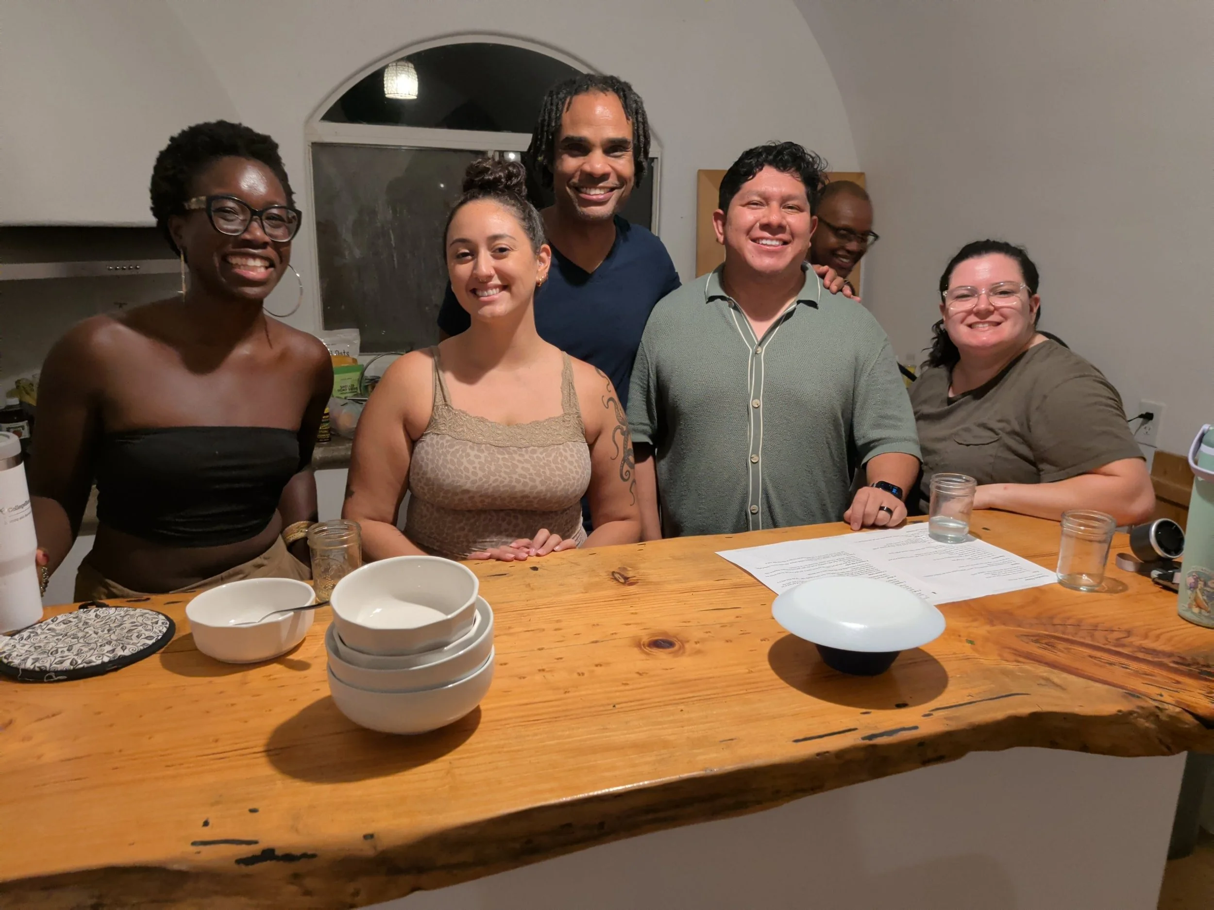 Kindred members smiling around a wooden kitchen table during an evening at the 2026 Kindred retreat