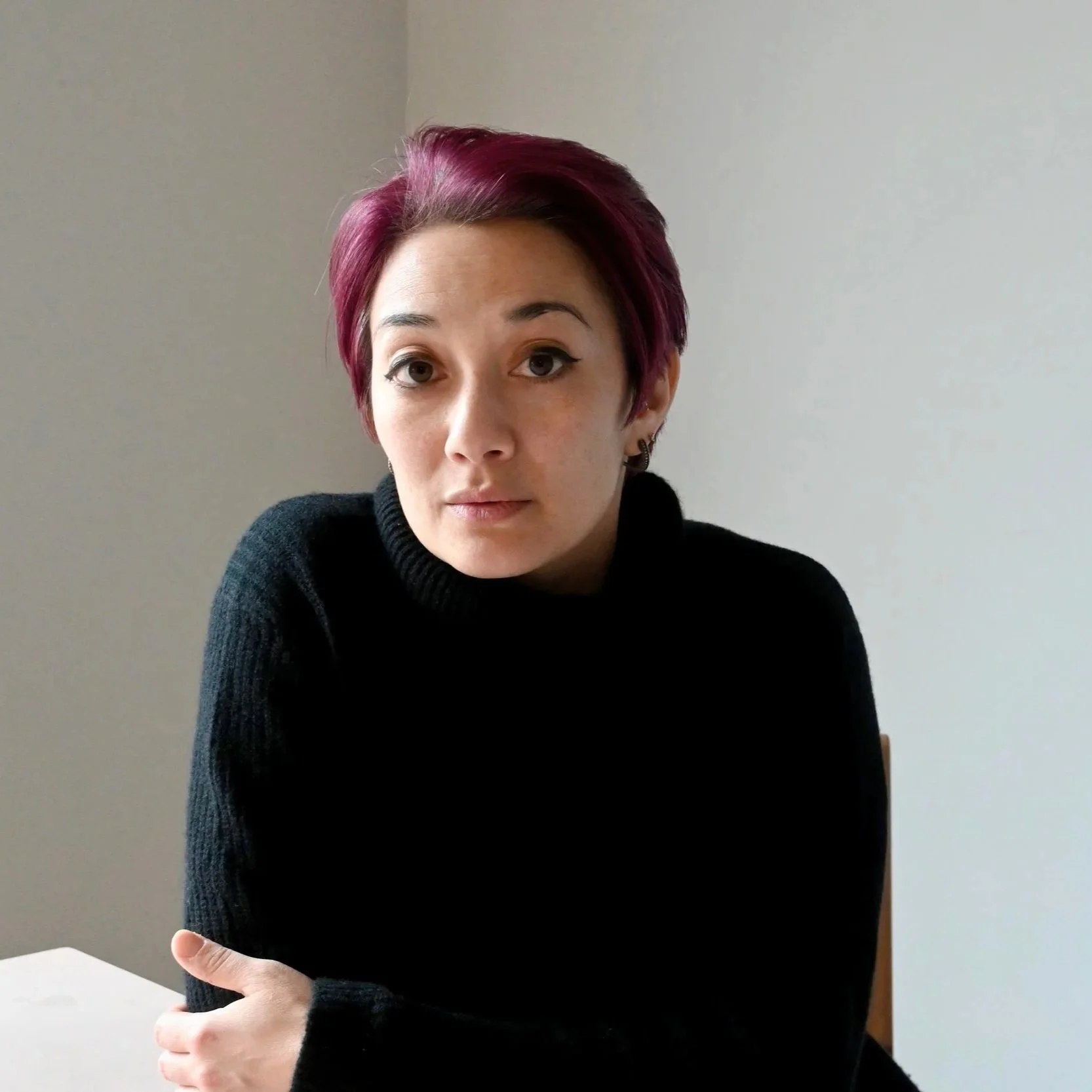 Headshot of a woman in a black sweater with pink hair.