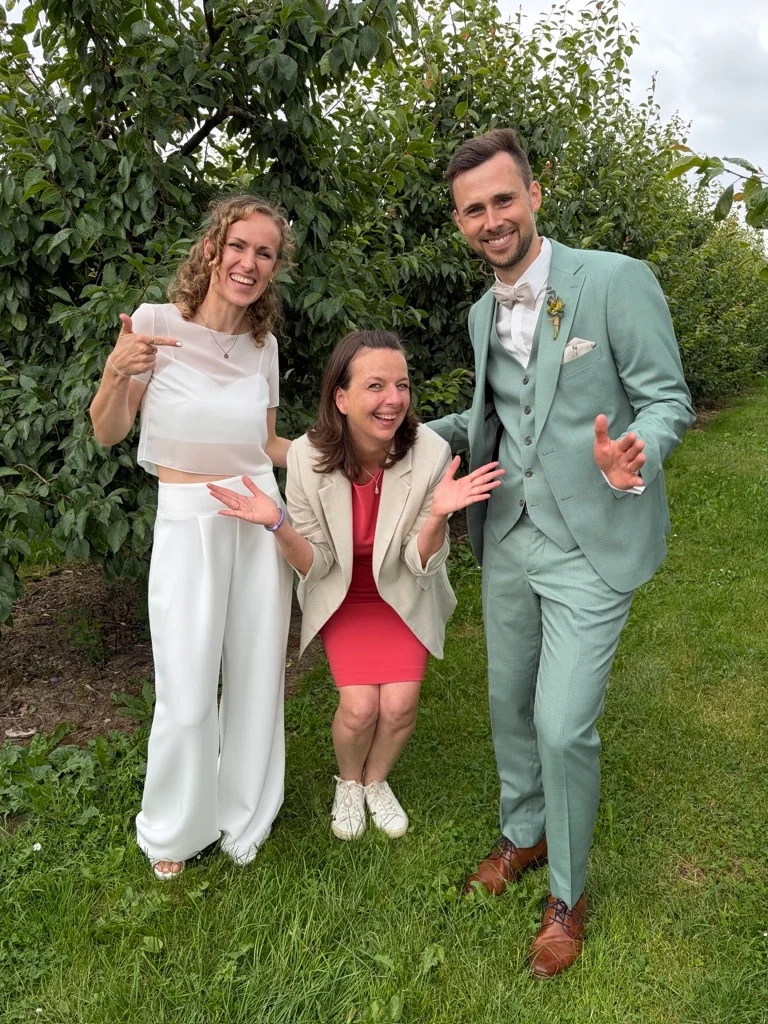 Drei Menschen lächeln und posieren im Garten, zwei Frauen und ein Mann in einem Anzug.
