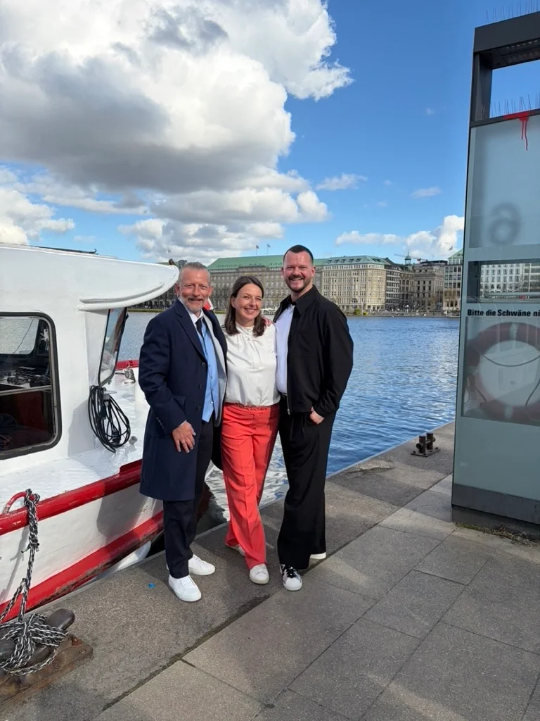 Schwules Hochzeitspaar mit Traurednerin Jana Henschel vor einer Alsterbarkasse in Hamburg