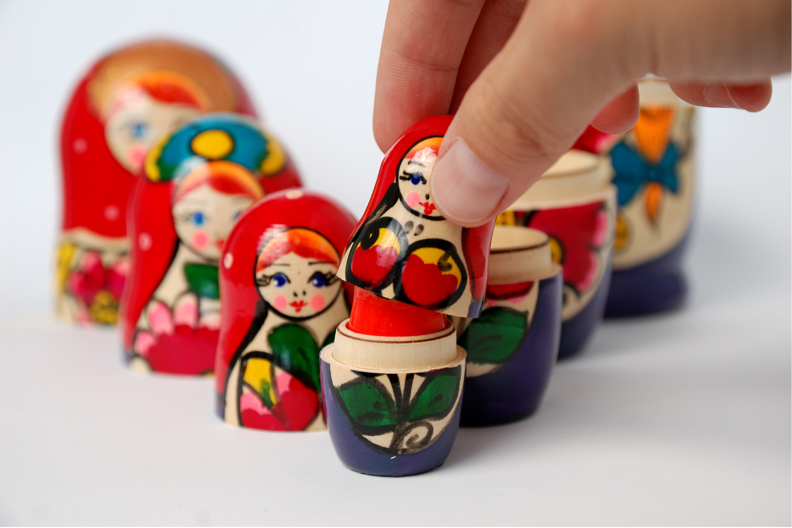A hand placing a painted Russian nesting doll onto a stack of similar dolls, with other dolls in the background. Family constellations - uncover hidden dynamics impacting your life.