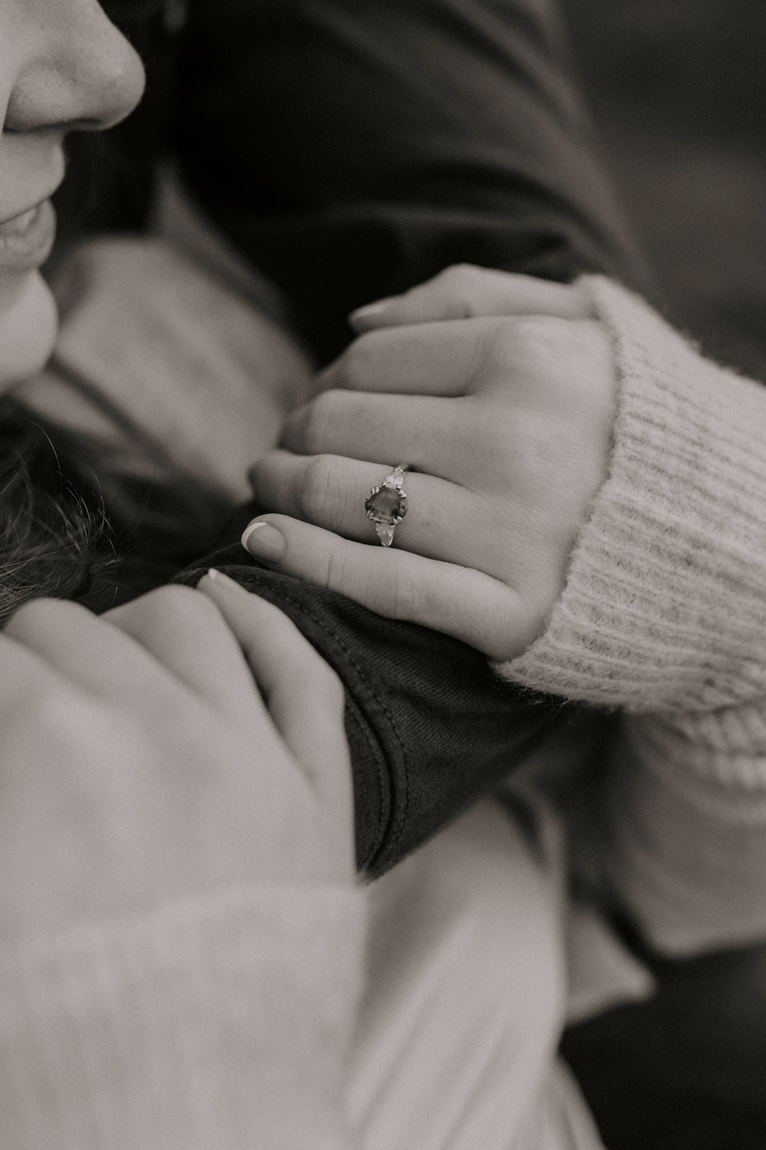 Close-up of a person wearing a ring on their finger, touching another person, in black and white.