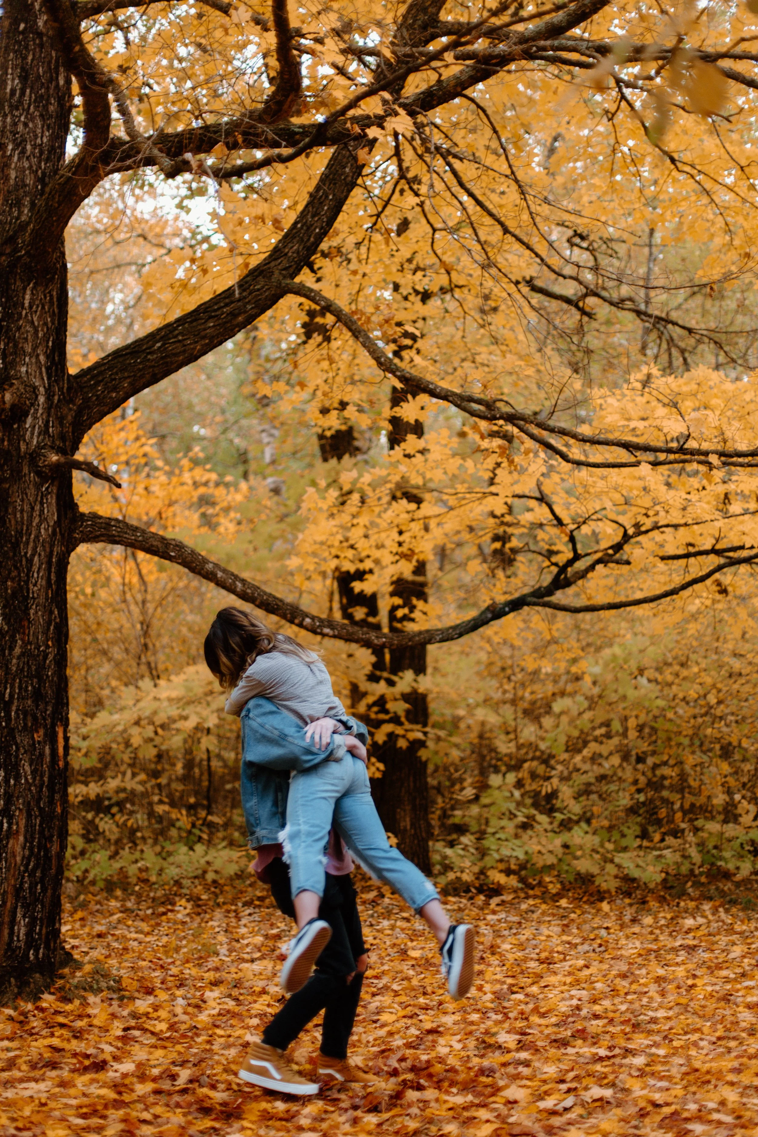 A person is lifting a child in the air in a forest with yellow autumn leaves.