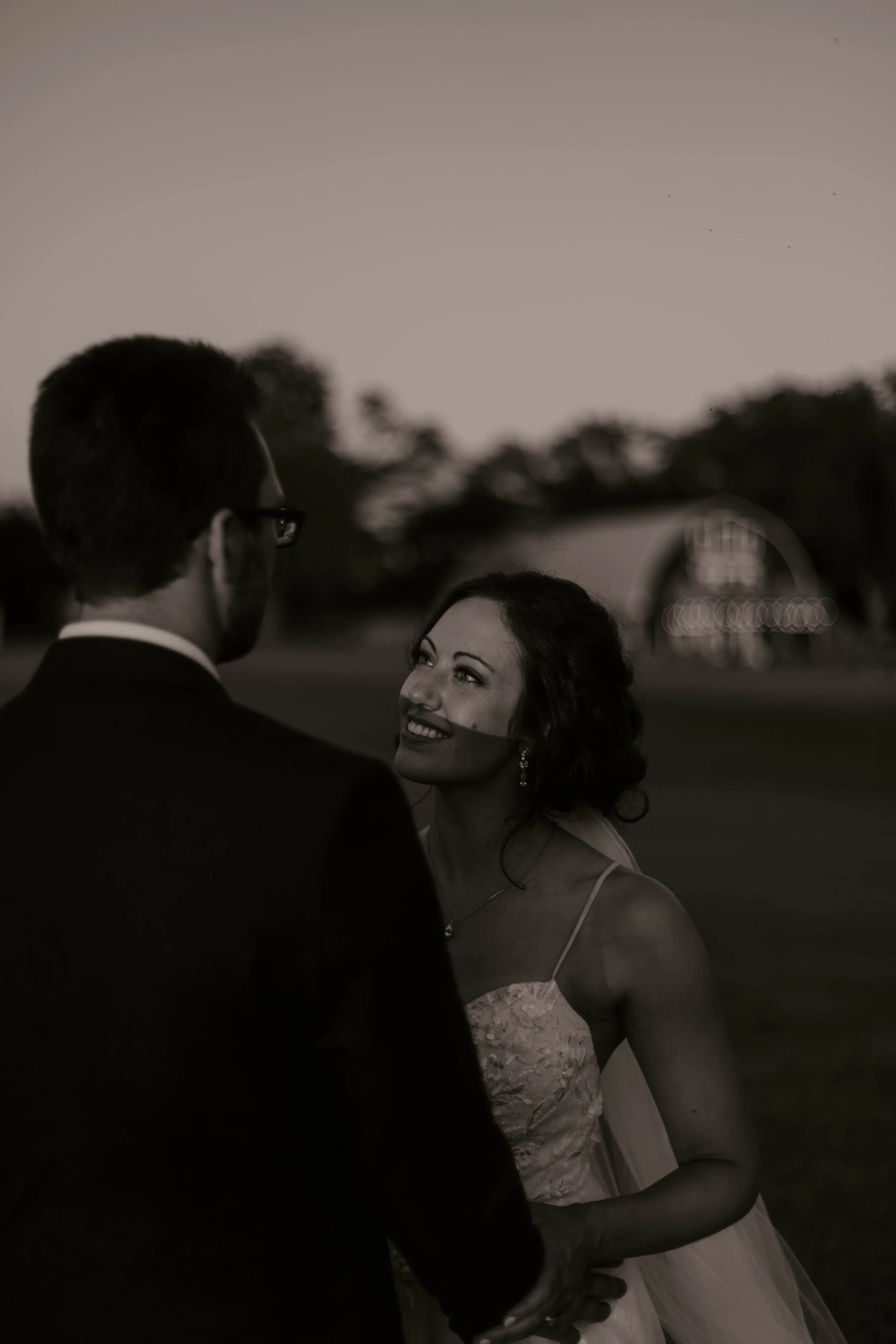 A couple holding hands, the woman is smiling and looking up at the man during sunset outdoors.
