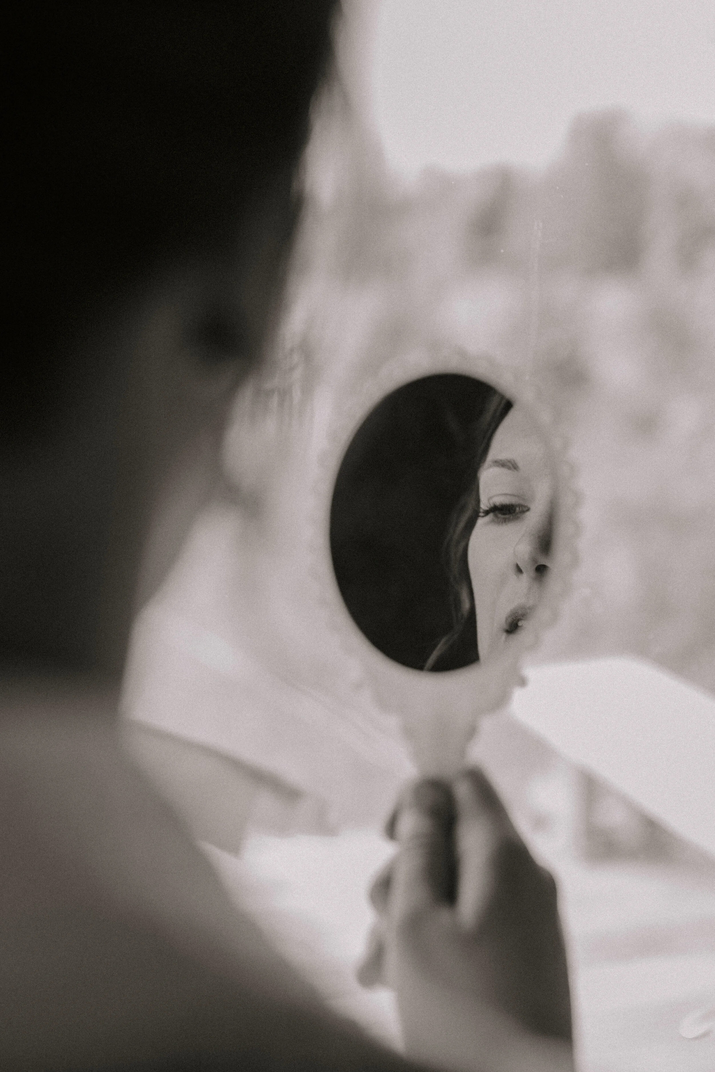 Close-up black and white abstract photograph of a person's face peering through a circular hole in paper, with focus on the eye and part of the nose.