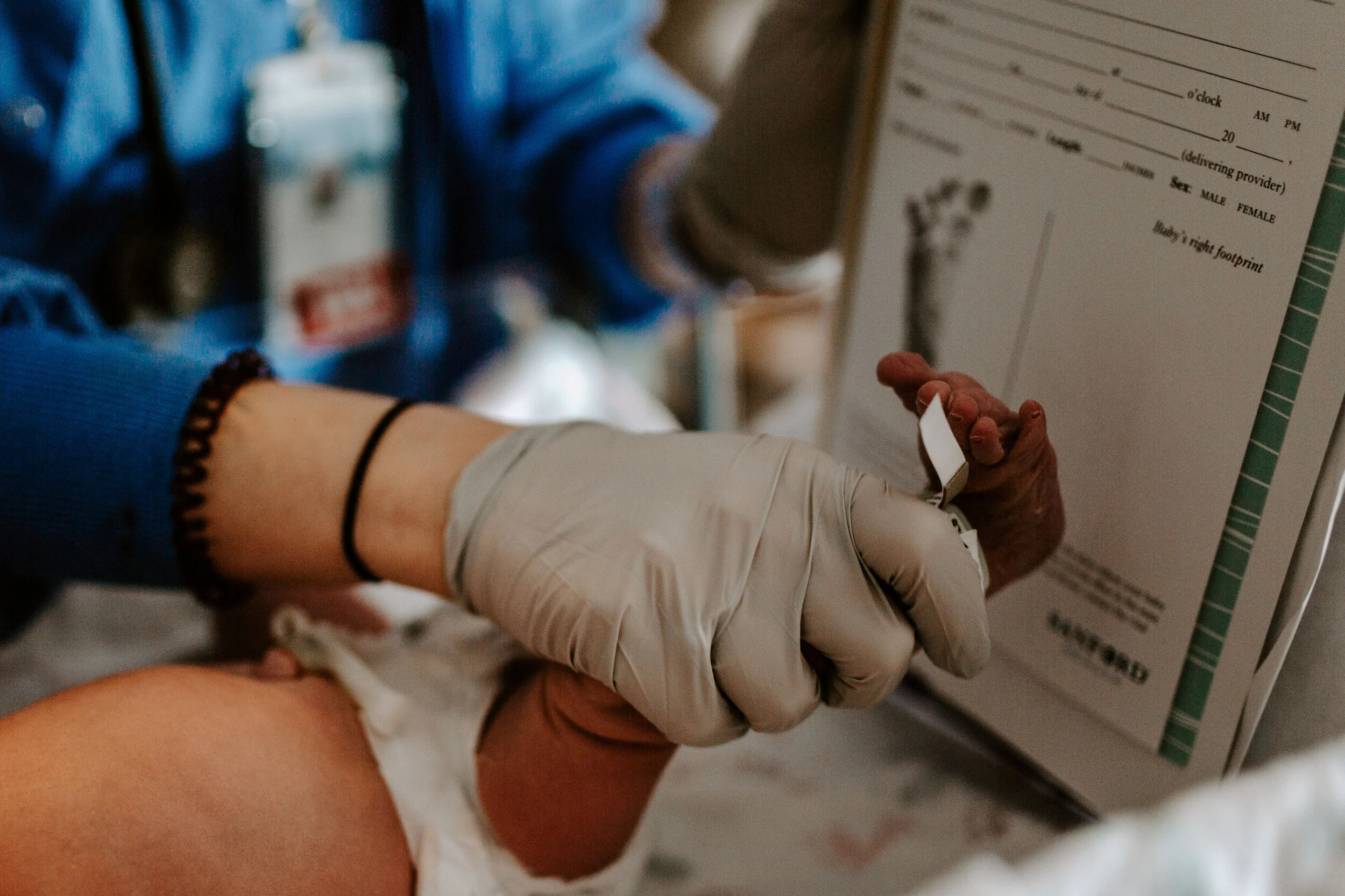 Close-up of a person's arm and hand with a white glove, holding a small vial or test tube, with a medical form or chart in the background.
