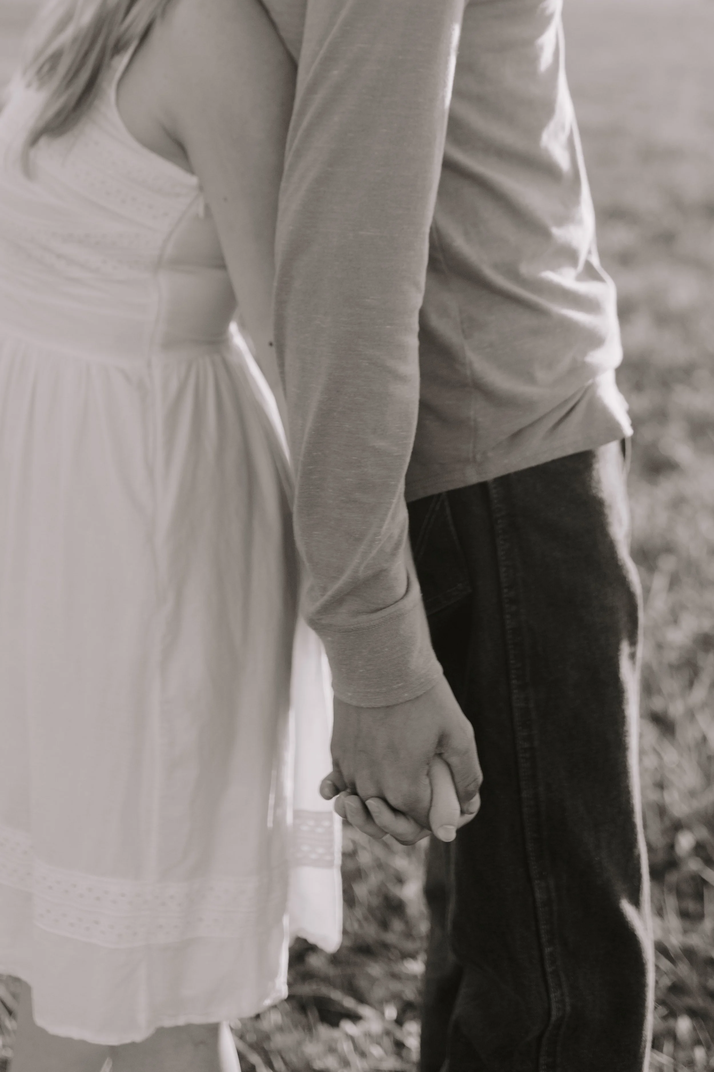 A close-up of two people holding hands, one wearing a white dress and the other wearing dark jeans and a light gray sweatshirt.