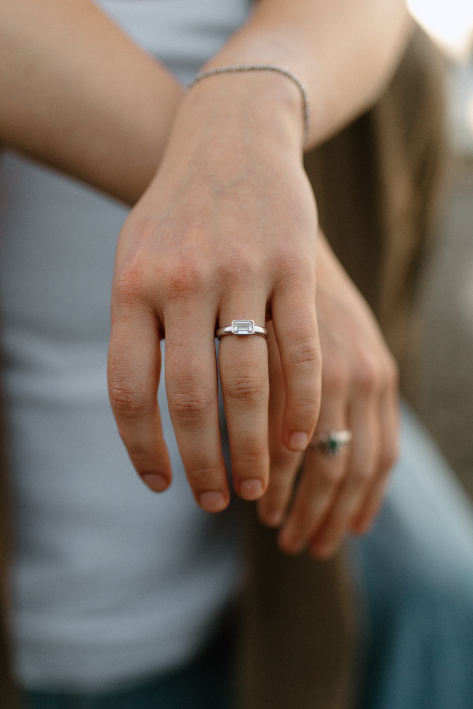 Close-up of a person's hand wearing a silver ring with a rectangular gemstone, resting on top of another person's hand.