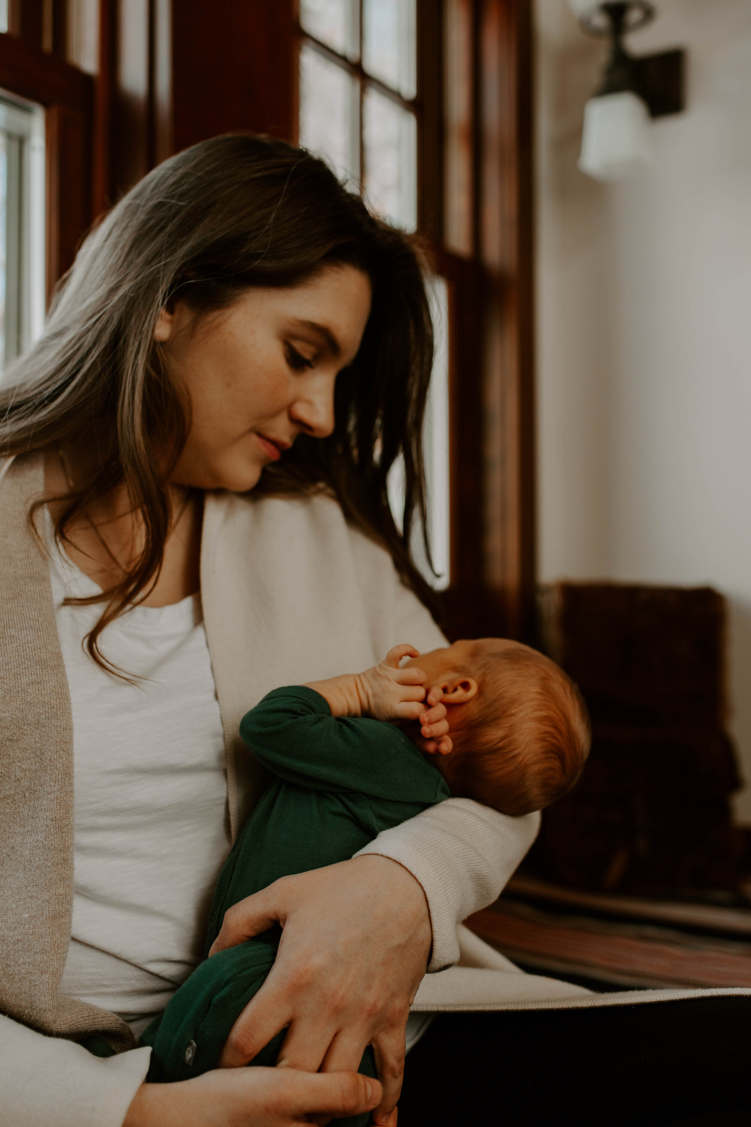 A woman holding a sleeping red-headed baby in her arms in a cozy room with wooden walls and windows.