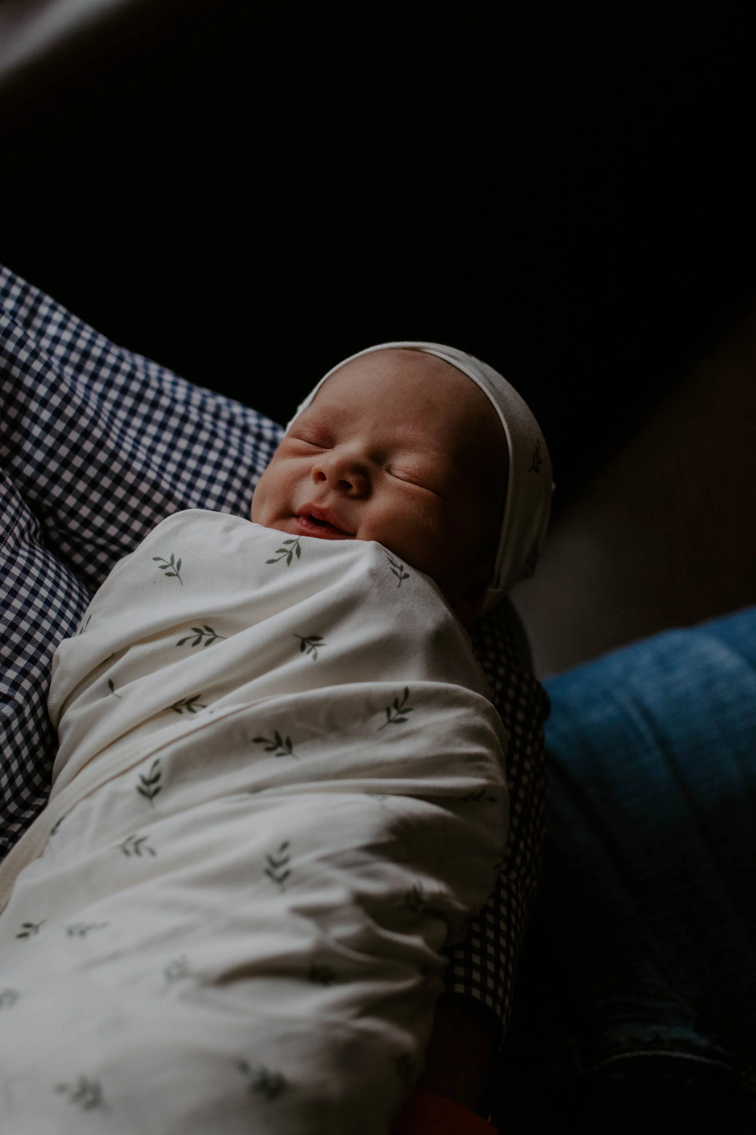 A sleeping baby wearing a white onesie with small green leaves, resting on an adult's lap.