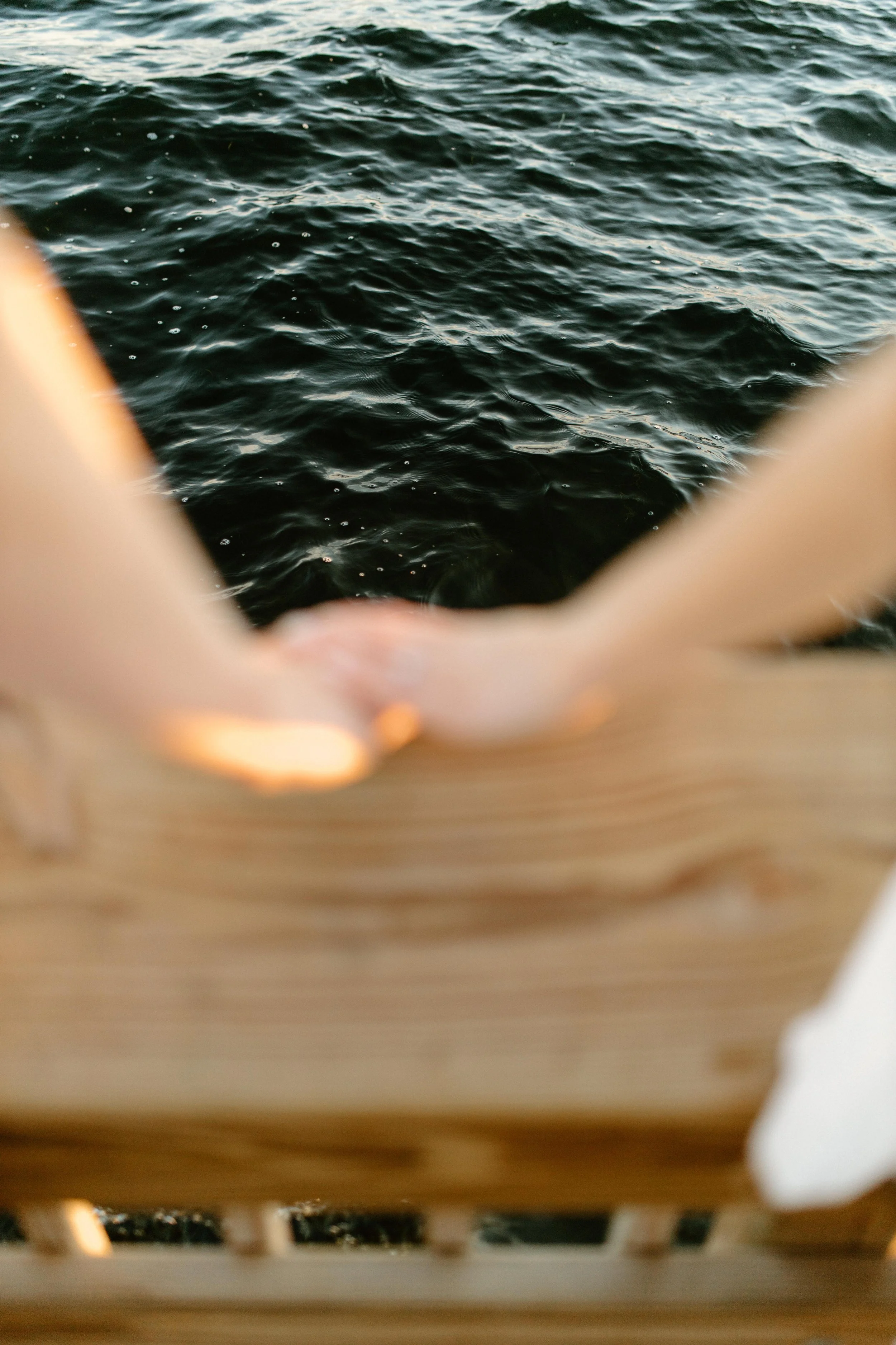 Close-up view of water through the slats of a wooden ship or dock, with blurred parts in the foreground.