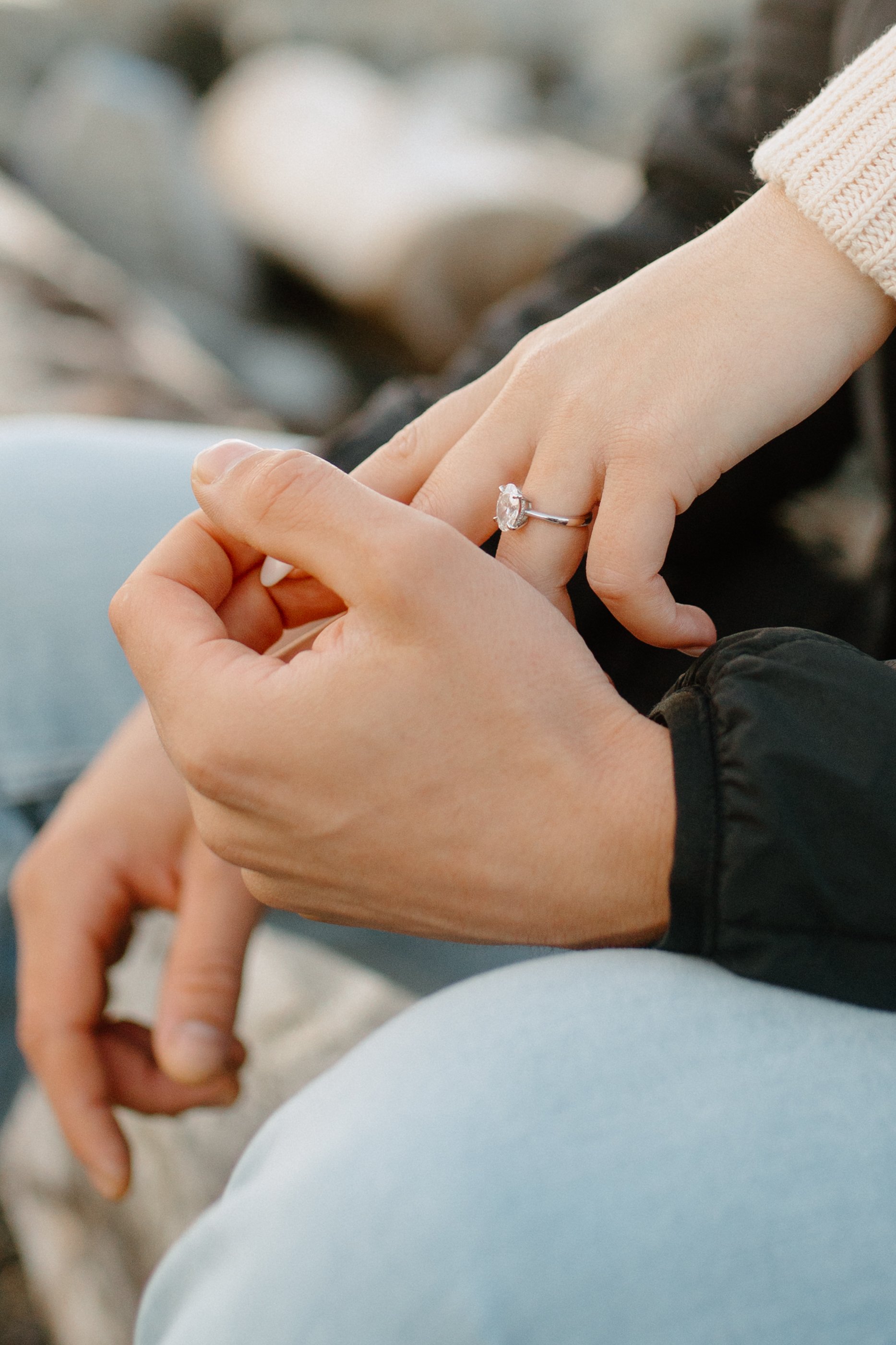 Close-up of a person wearing a silver ring with a large oval-shaped gemstone on their finger, resting their hand on another person's knee.