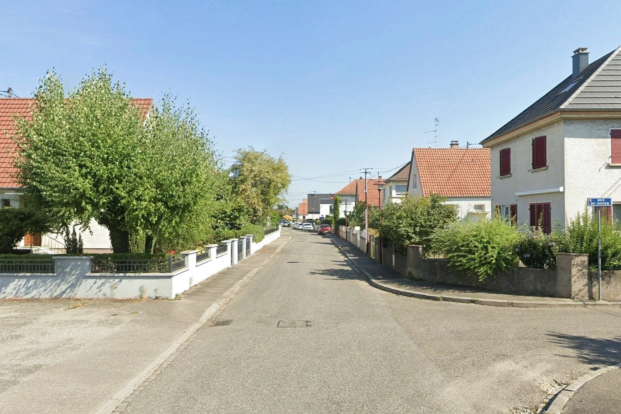 Rue résidentielle avec maisons et arbres sous un ciel clair.