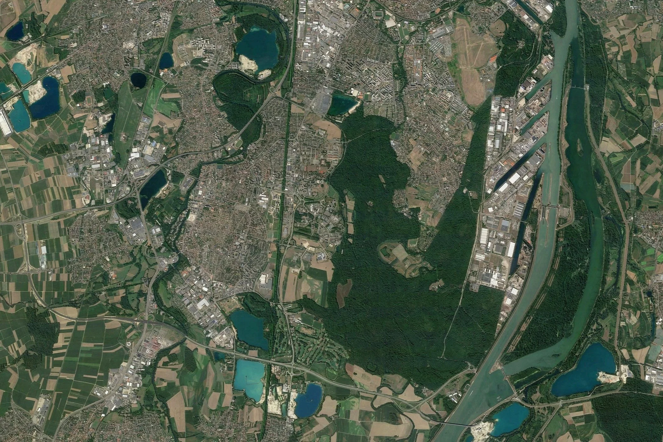 Vue aérienne d'une région urbaine avec des quartiers résidentiels, des zones industrielles, des plans d'eau, et une grande rivière.