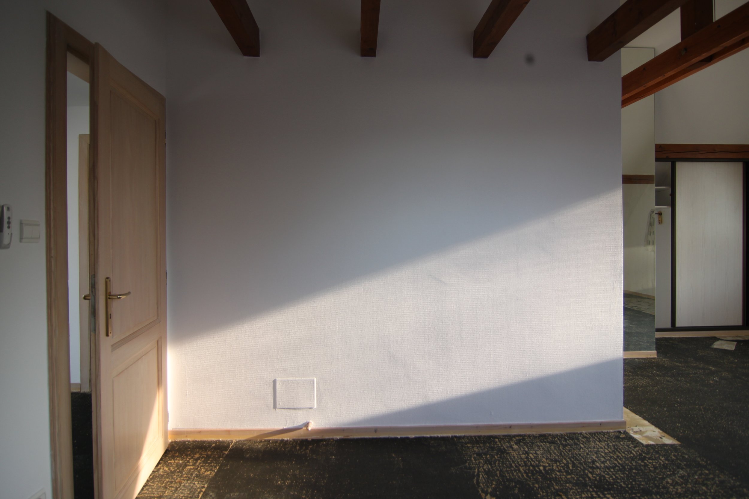 Mur blanc avec une ouverture lumineuse laissant passer la lumière du soleil, intérieur d'une pièce avec porte en bois et parquet.