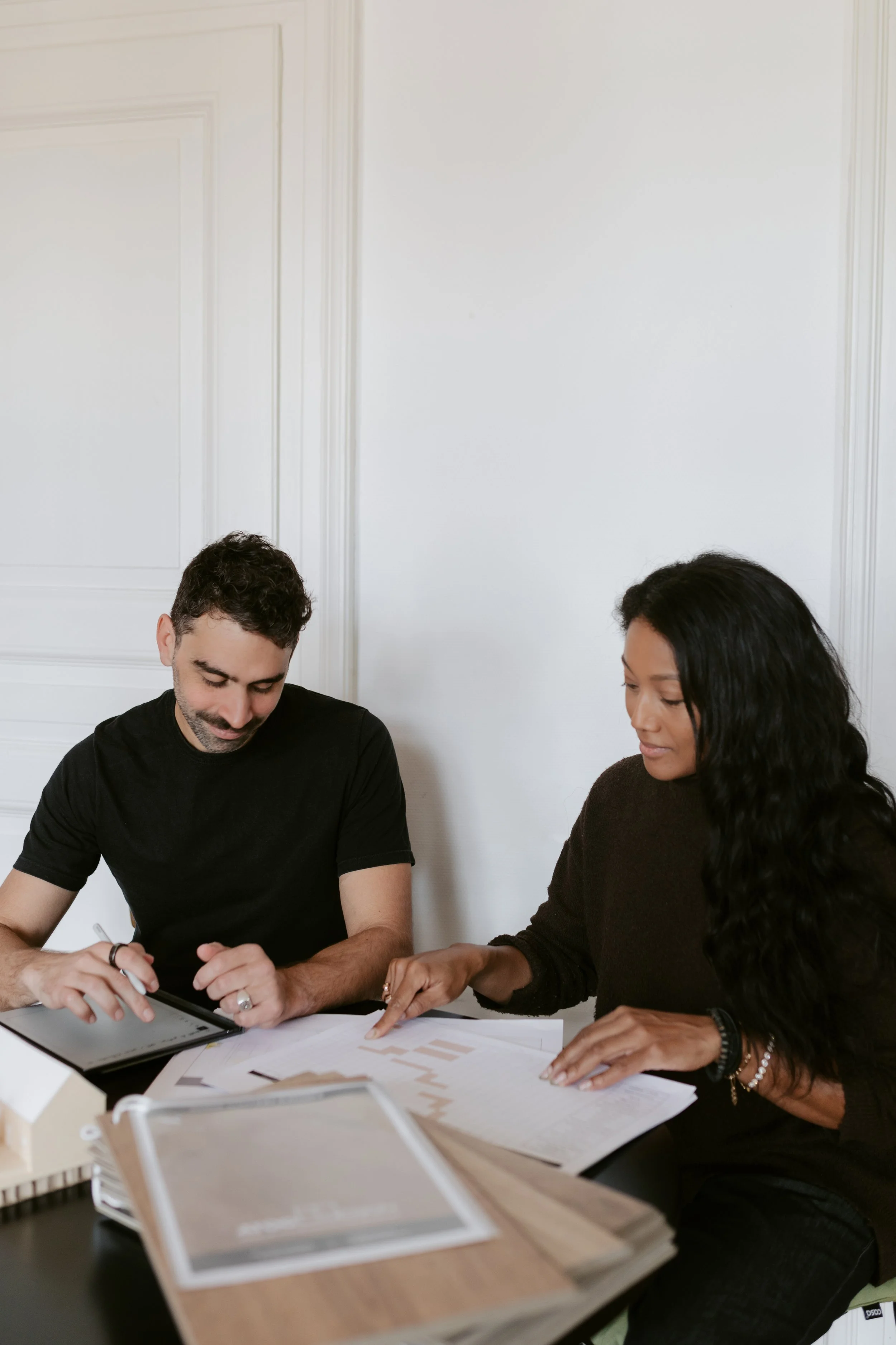 Deux personnes, un homme et une femme, discutent et examinent des documents et un tableau numérique lors d'une réunion.