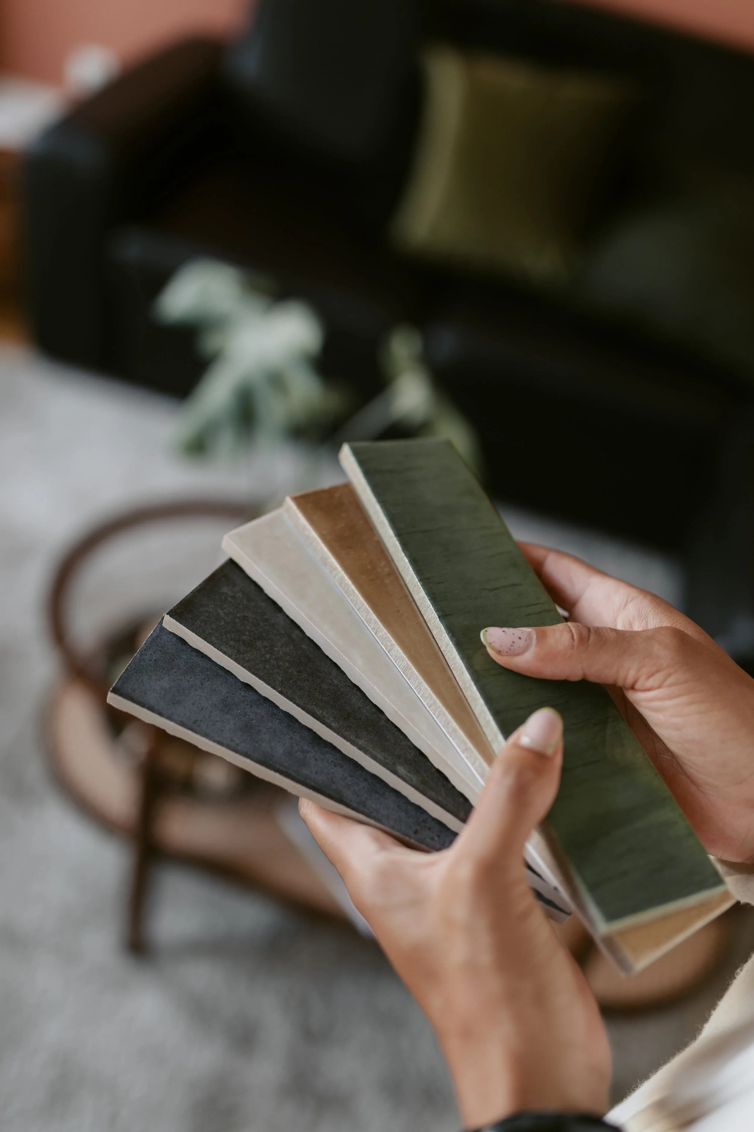 Grosse main tenant six échantillons de matériaux de différentes couleurs et textures, avec un canapé en arrière-plan.