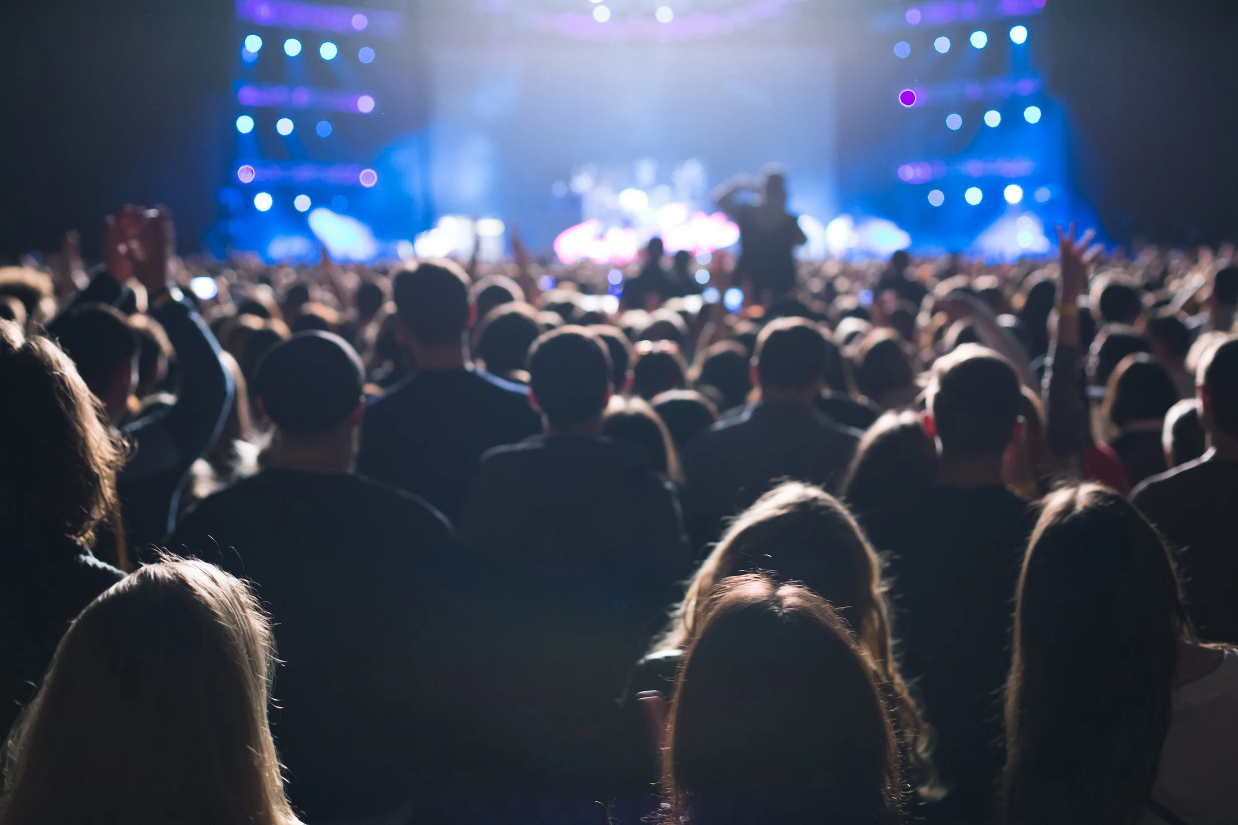 The back view of a crowd looking at a performance on a stage that's lit up blue