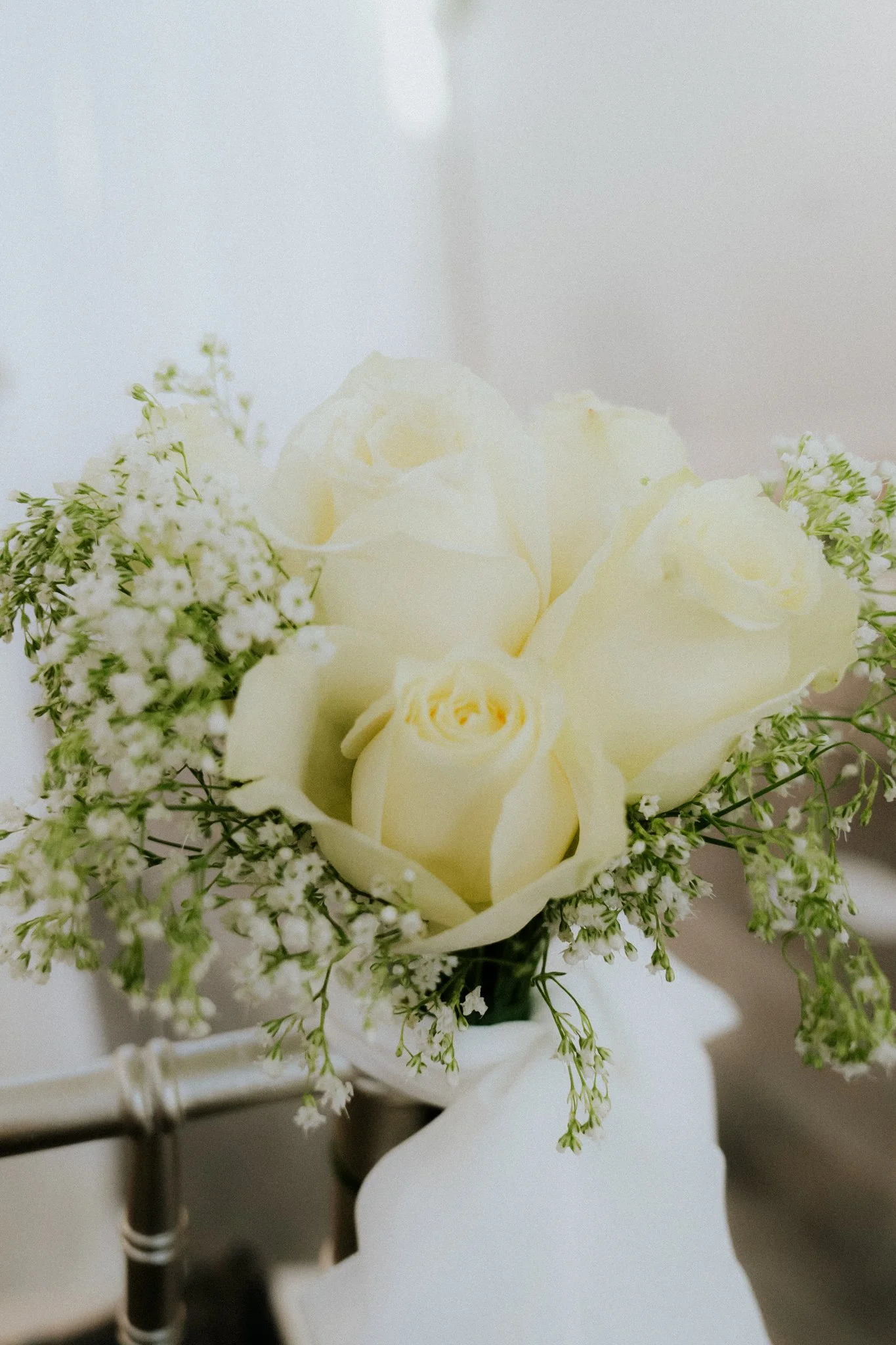 A bouquet of white roses and small white flowers in a white vase.