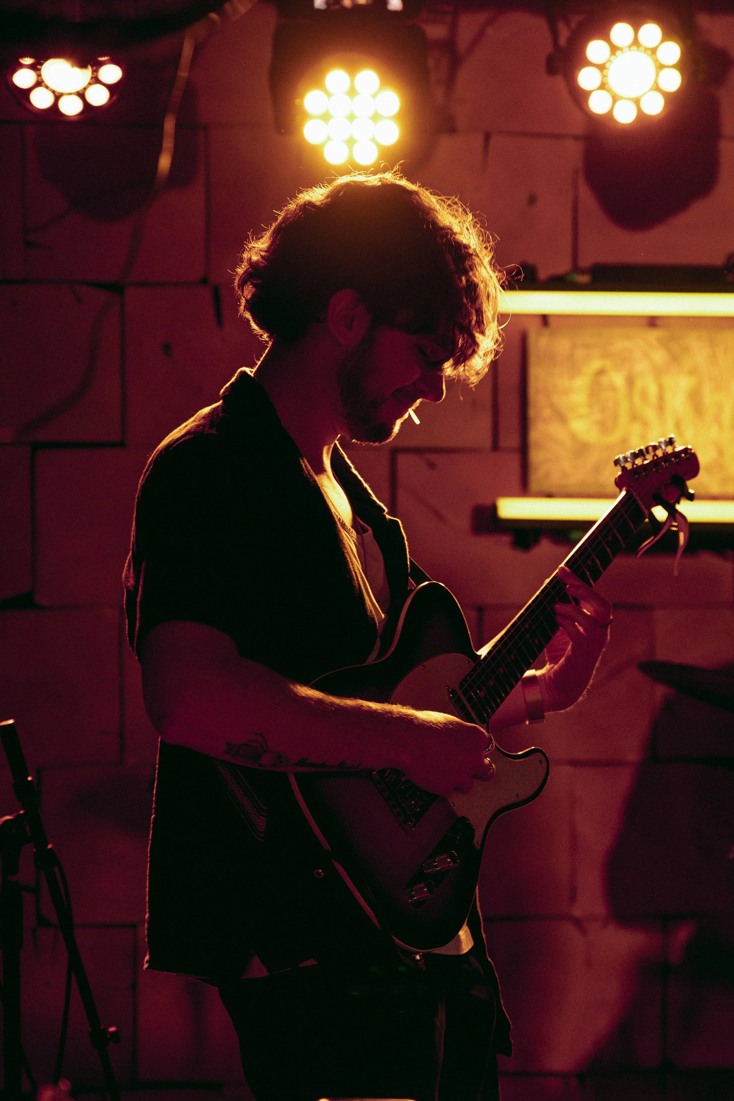 A silhouette of a young man playing an electric guitar on stage under warm, colorful lights.