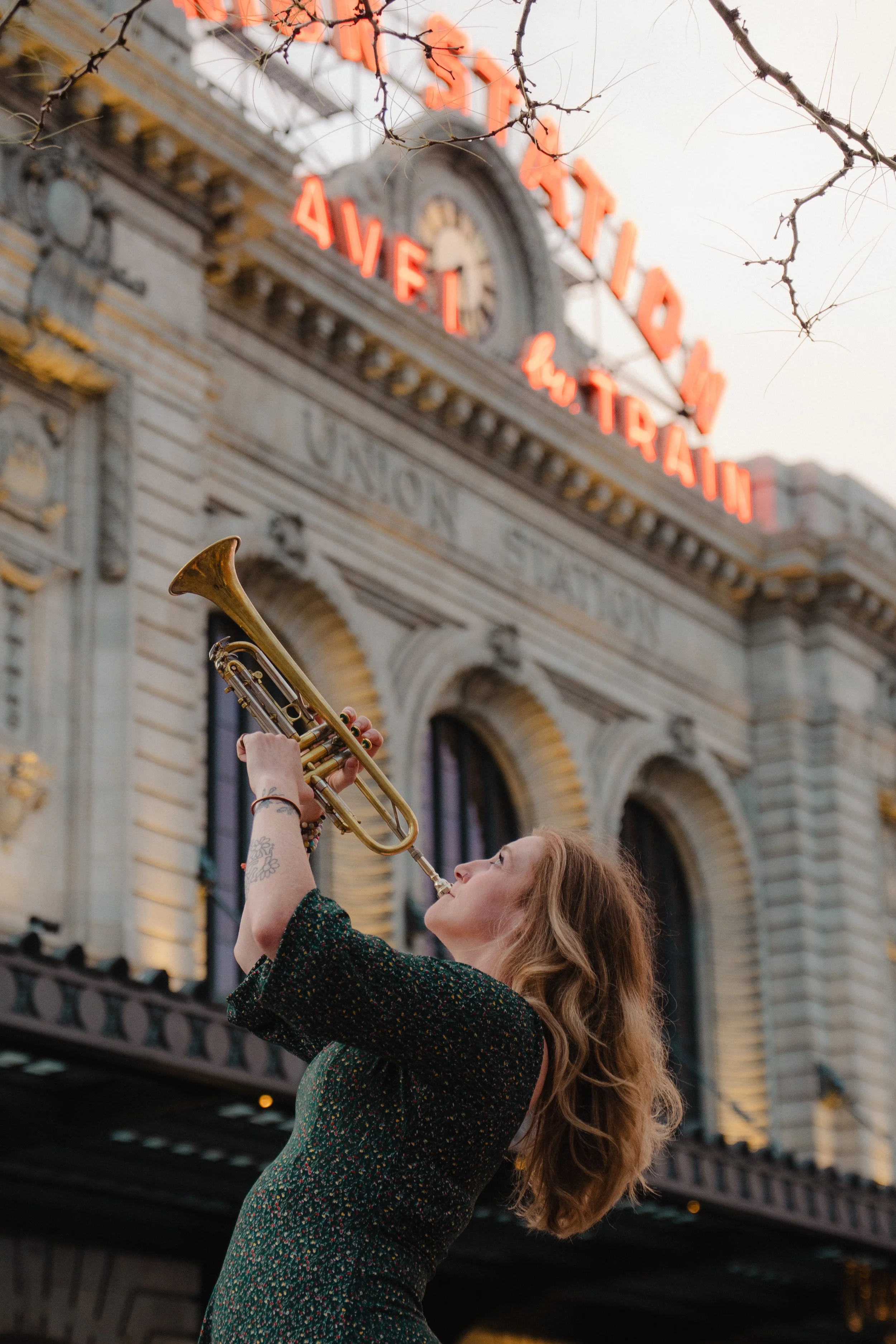 A woman playing a trumpet outdoors in front of Union Station with illuminated sign reading 'Union Station' in the background.