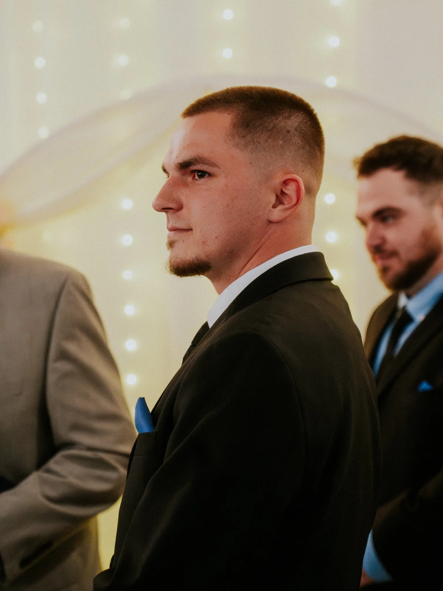 A young man in a black suit with a blue pocket square attending a formal event.