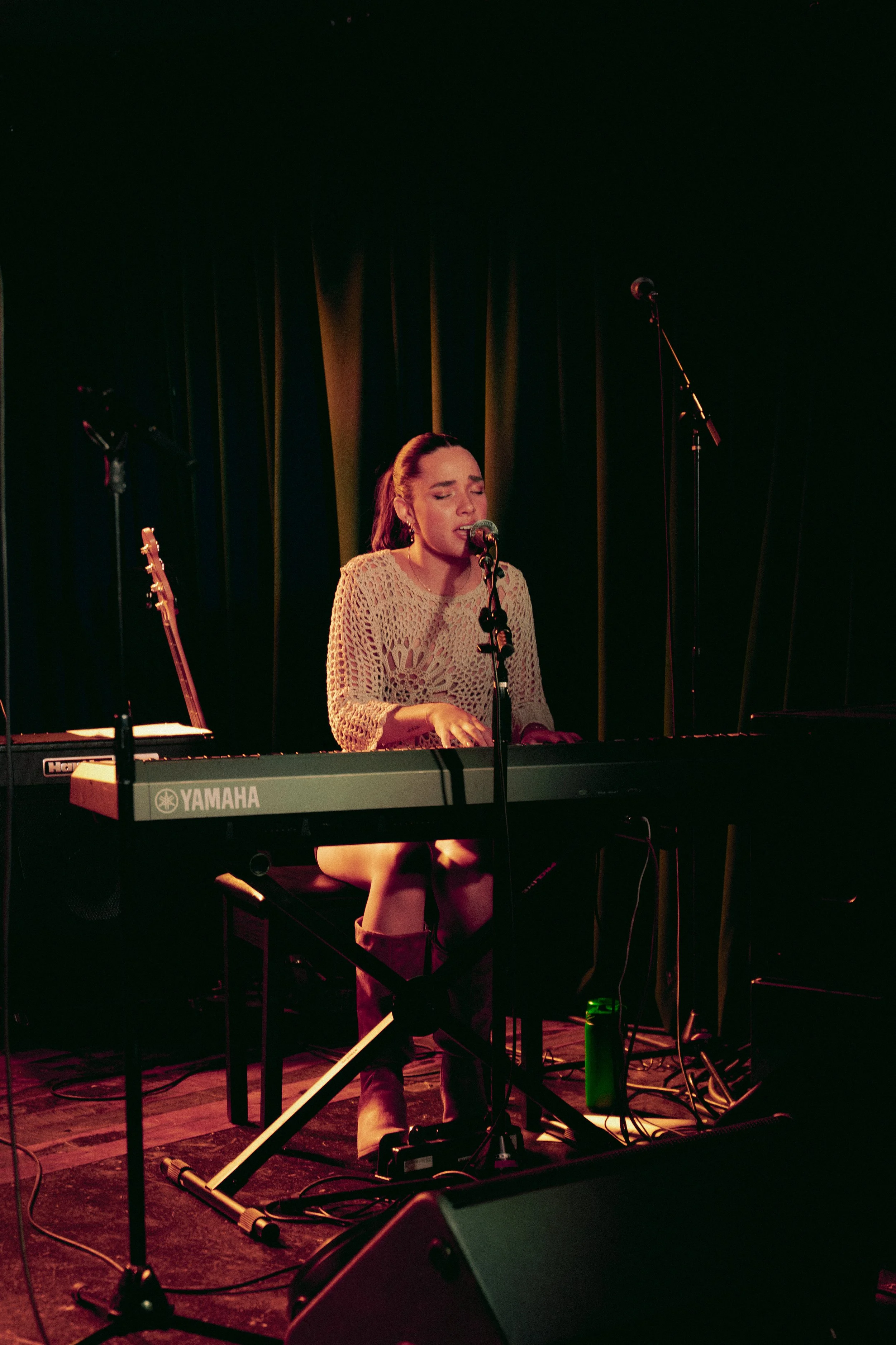 A woman singing and playing a Yamaha keyboard on stage with dark curtains in the background.