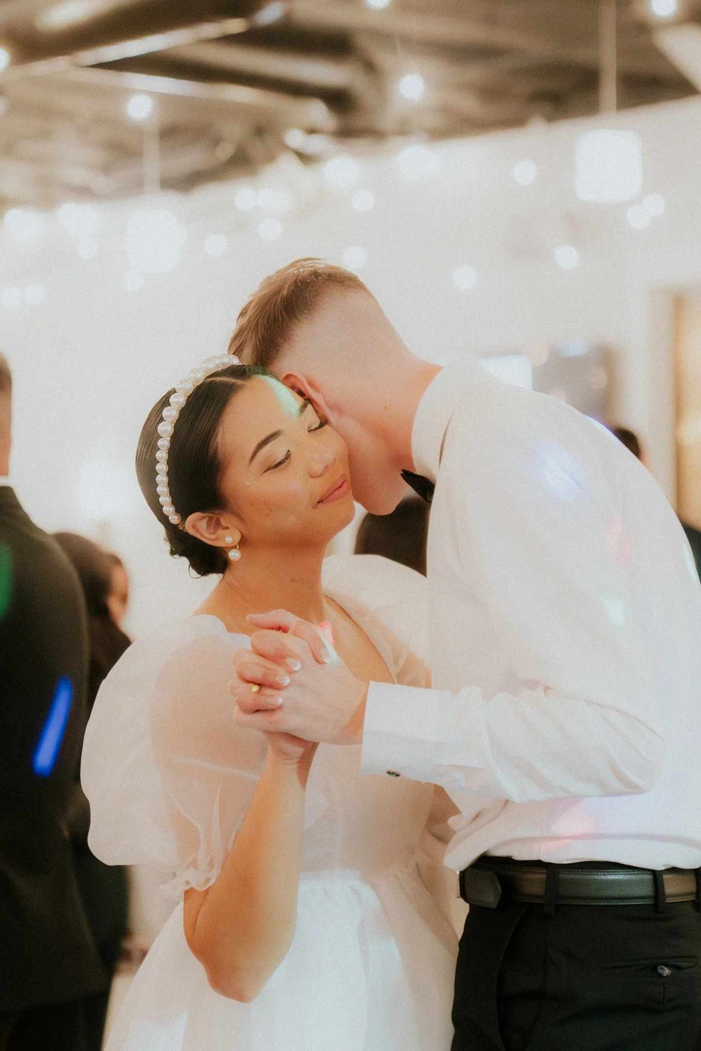 A woman with dark hair and pearl headband dancing with a man in a white shirt at a wedding reception.