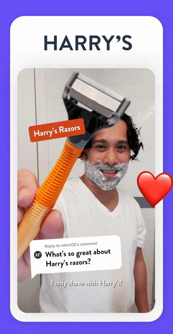 A man with curly hair and a beard shaving with Harry's razors, holding a yellow razor head close to the camera, with foam on his face, standing in a bathroom.