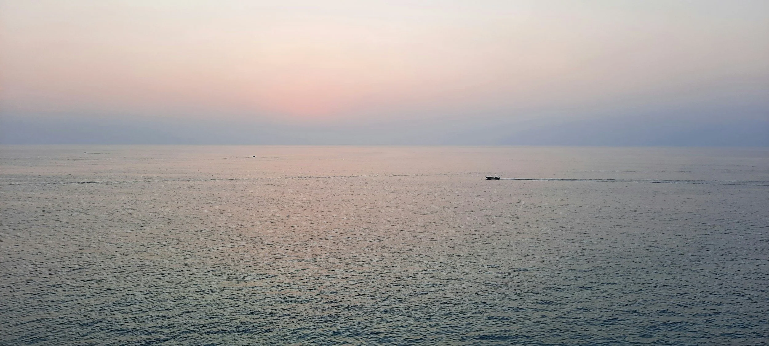 Calm ocean horizon at sunrise with a small boat moving across still water, symbolizing reflection and the practice of beginning again.