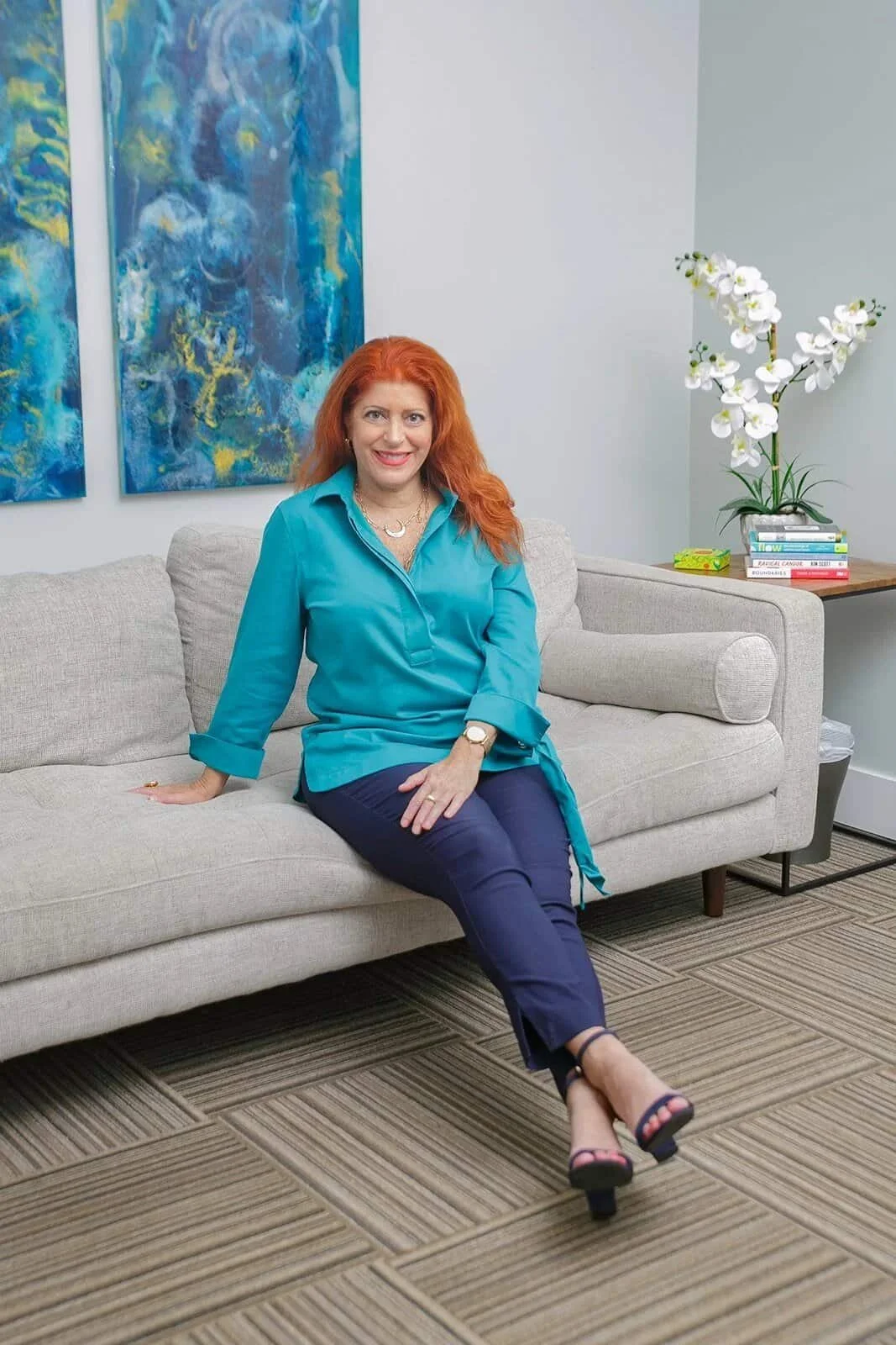 woman with red hair and blue top sitting on a grey couch