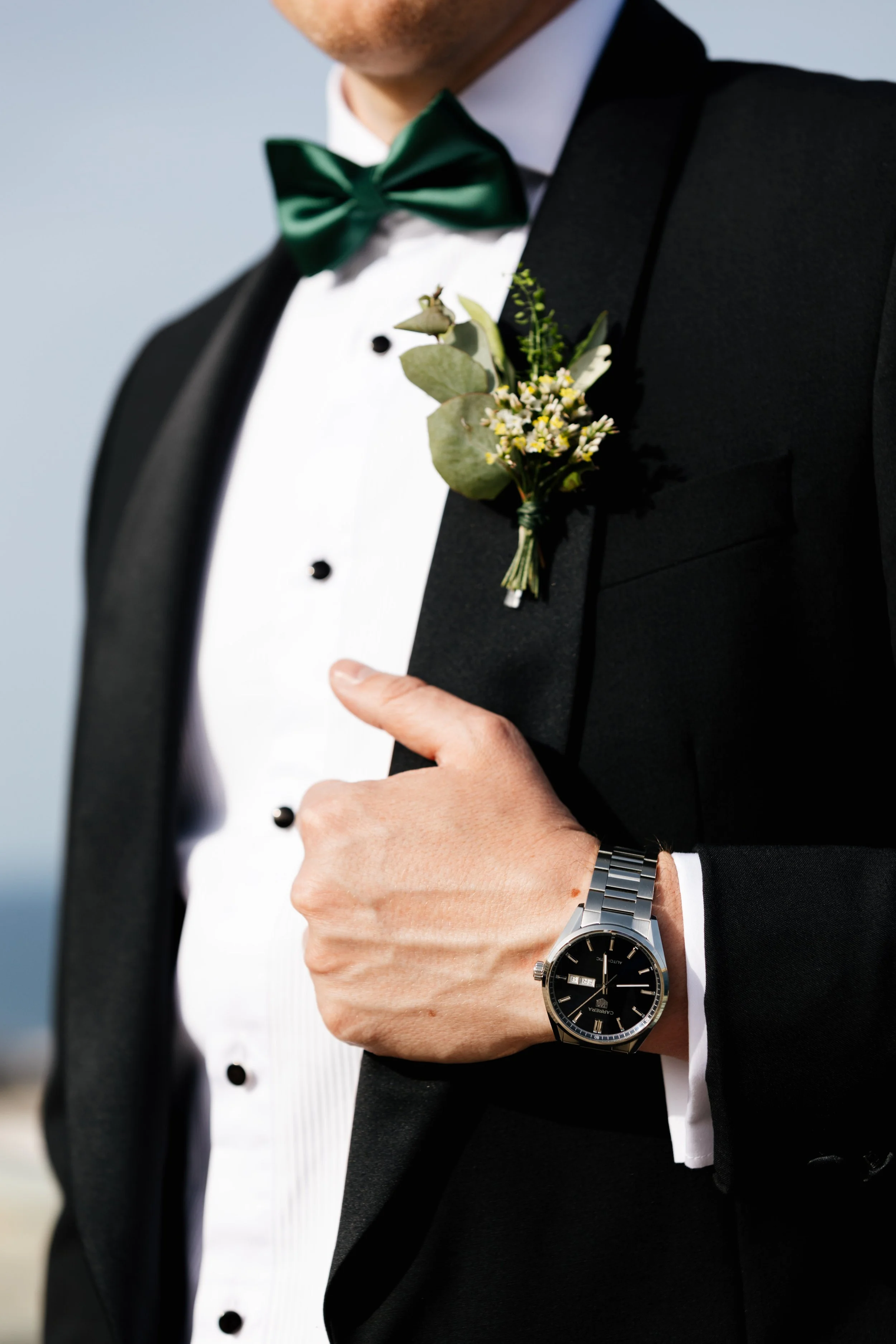 Man in formal suit with boutonniere and wristwatch, adjusting jacket